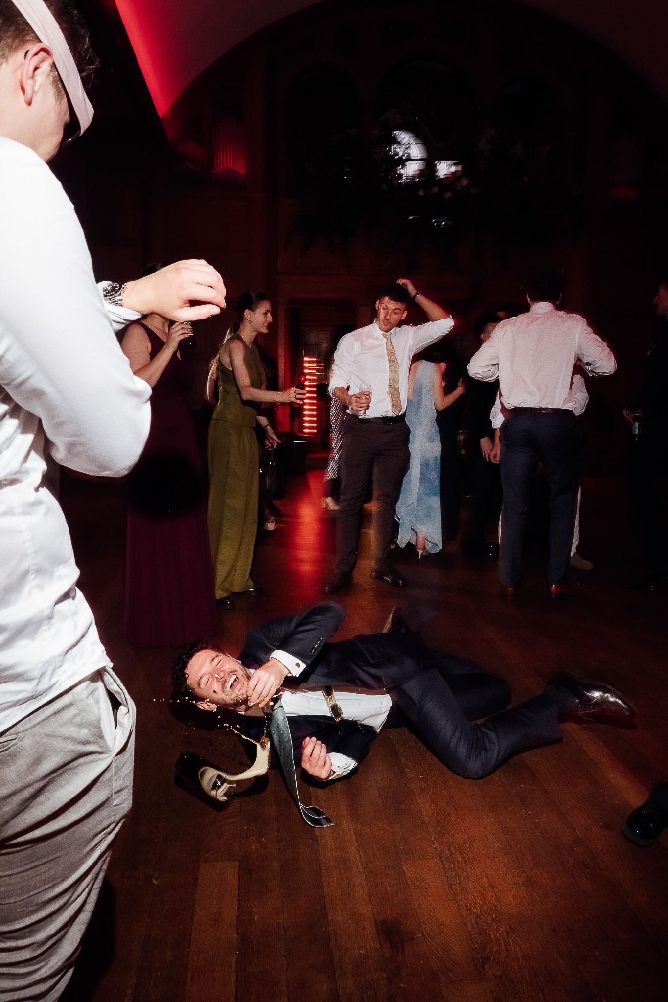 Guests dancing at a wedding reception, with one man lying on the floor laughing in a navy suit.