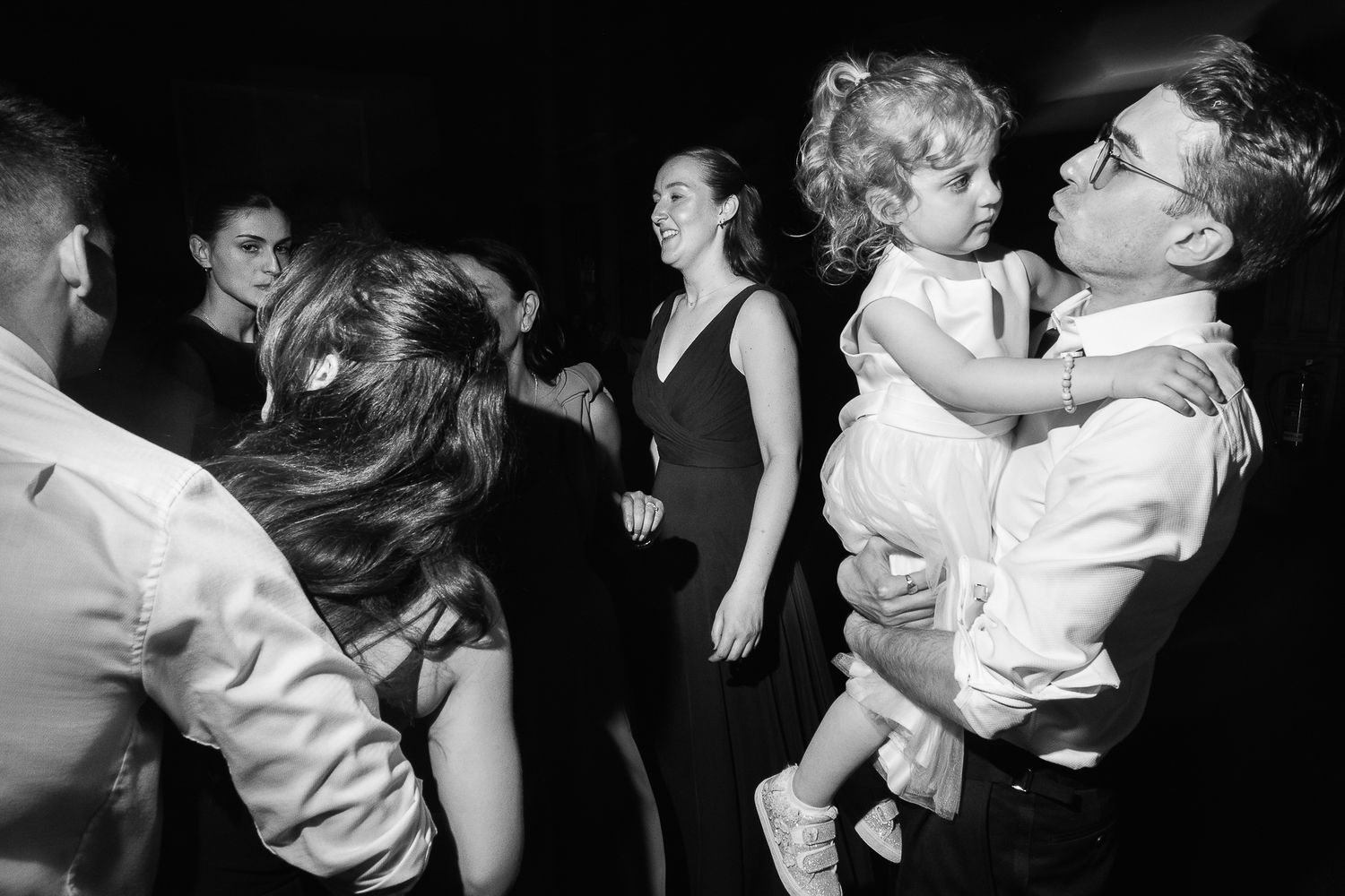 Black and white photo of adults and a child dancing joyfully at a wedding reception party.