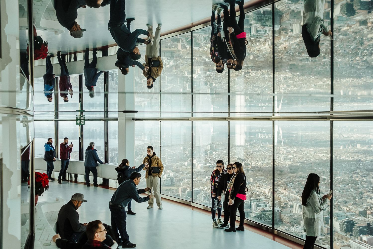 People walk through a mirrored ceiling art installation creating a surreal upside-down reflection effect.