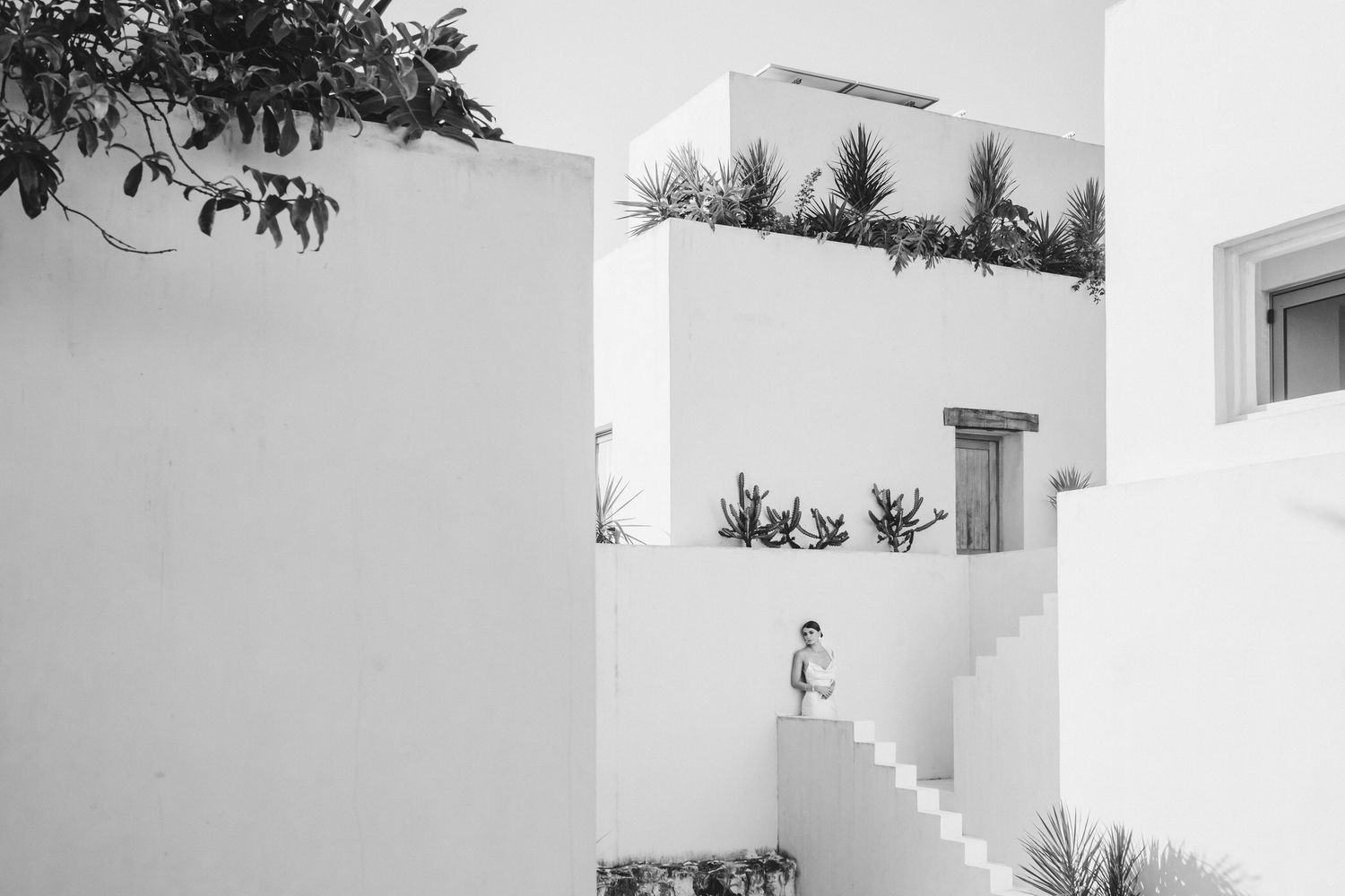 Black and white architectural photograph showing minimalist white buildings with clean geometric lines and shadows.
