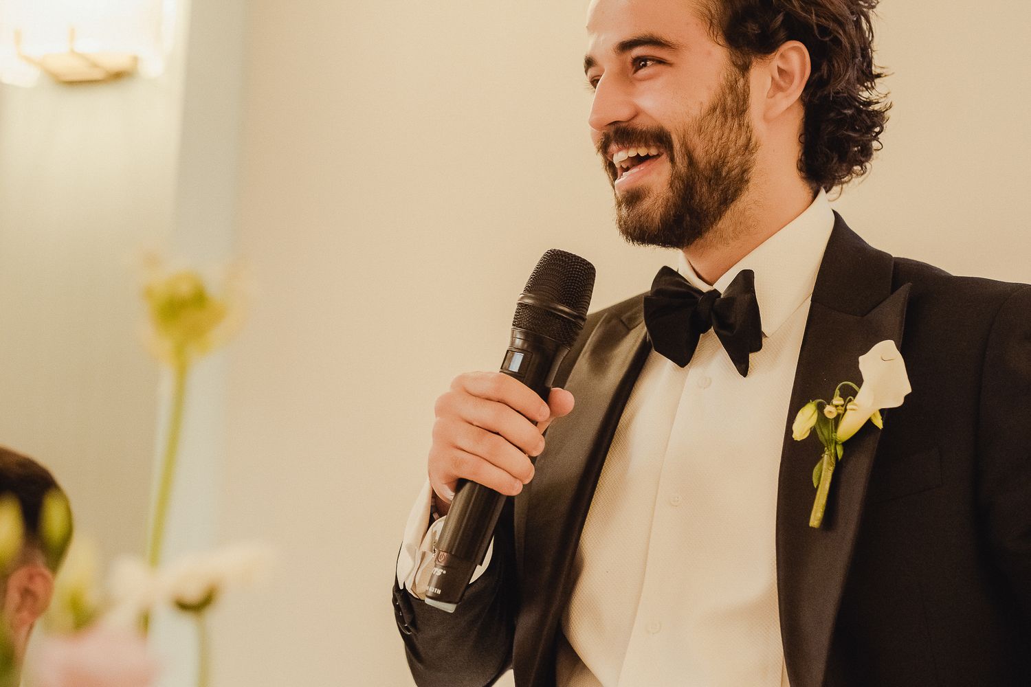 Wedding guests smile and laugh during an emotional reception toast at an elegant indoor venue.