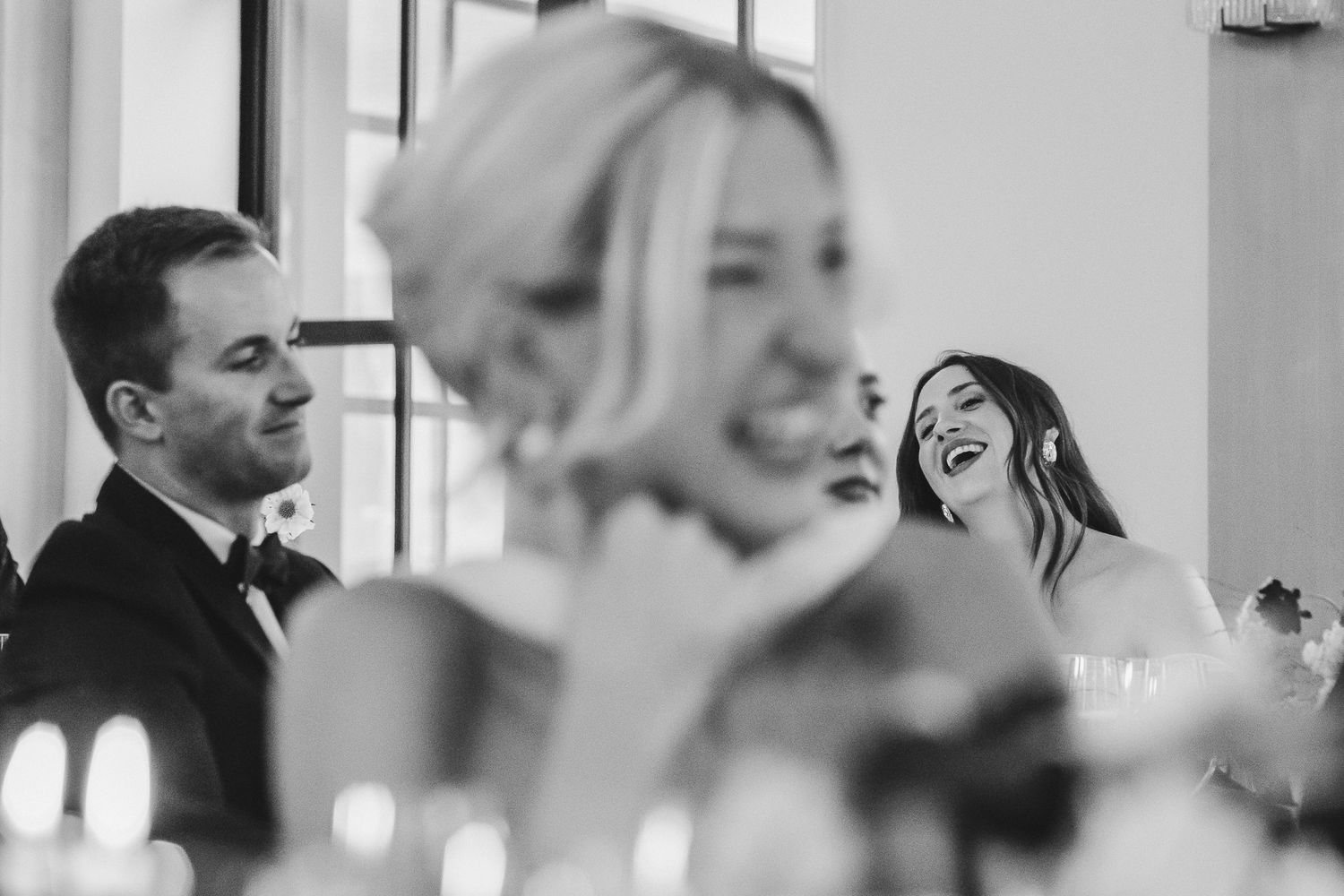 Black and white candid photo of guests laughing and enjoying themselves during a wedding reception.