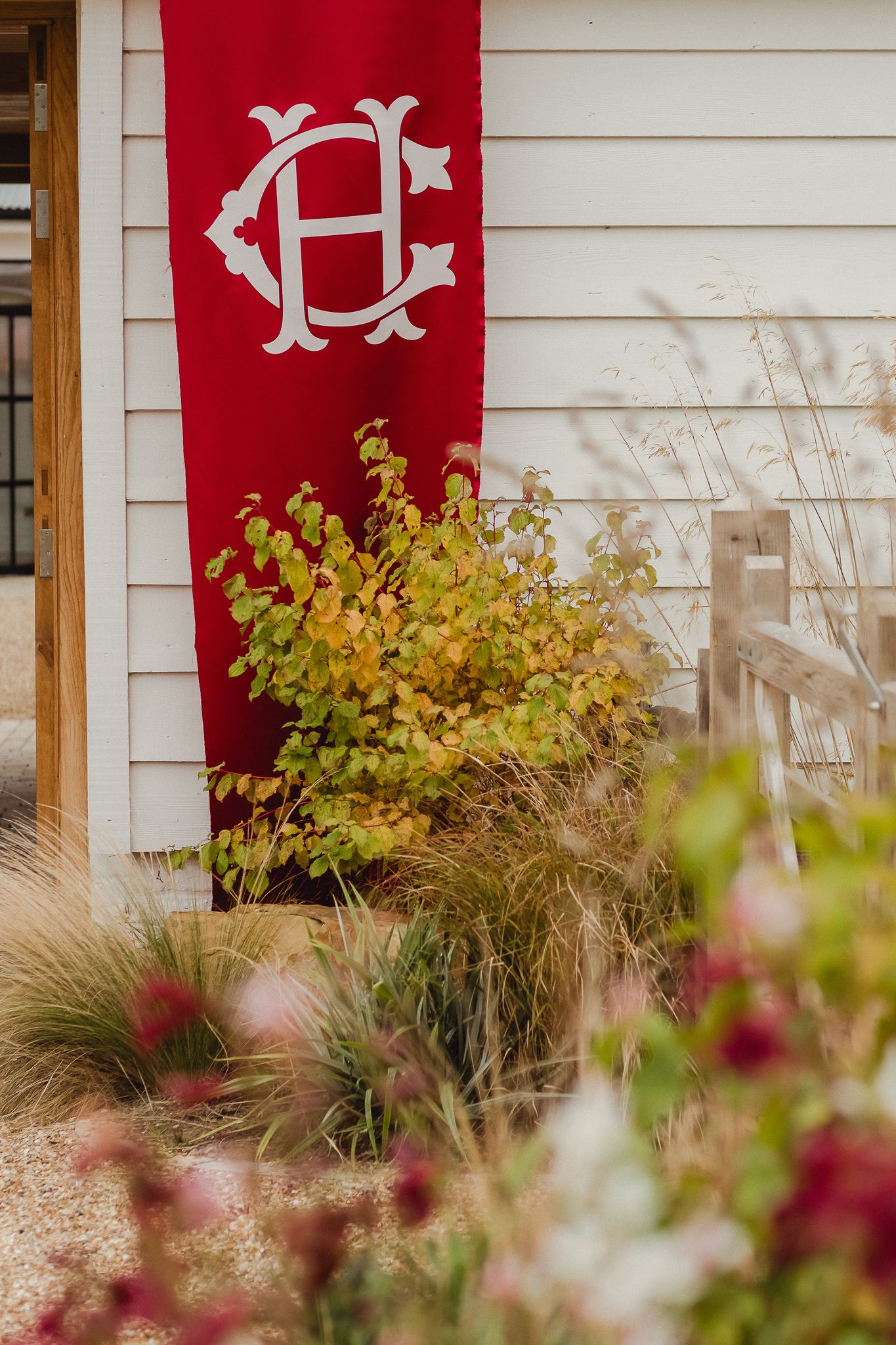 Red decorative banners with ornate designs hang against white siding, with green foliage and flowers in the foreground.