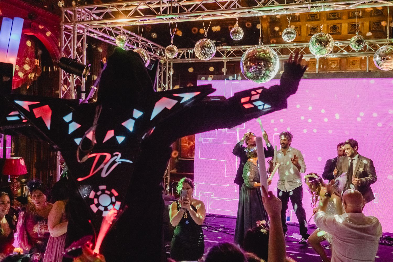 A group of performers on stage entertain guests at what appears to be a wedding reception with colorful lighting.