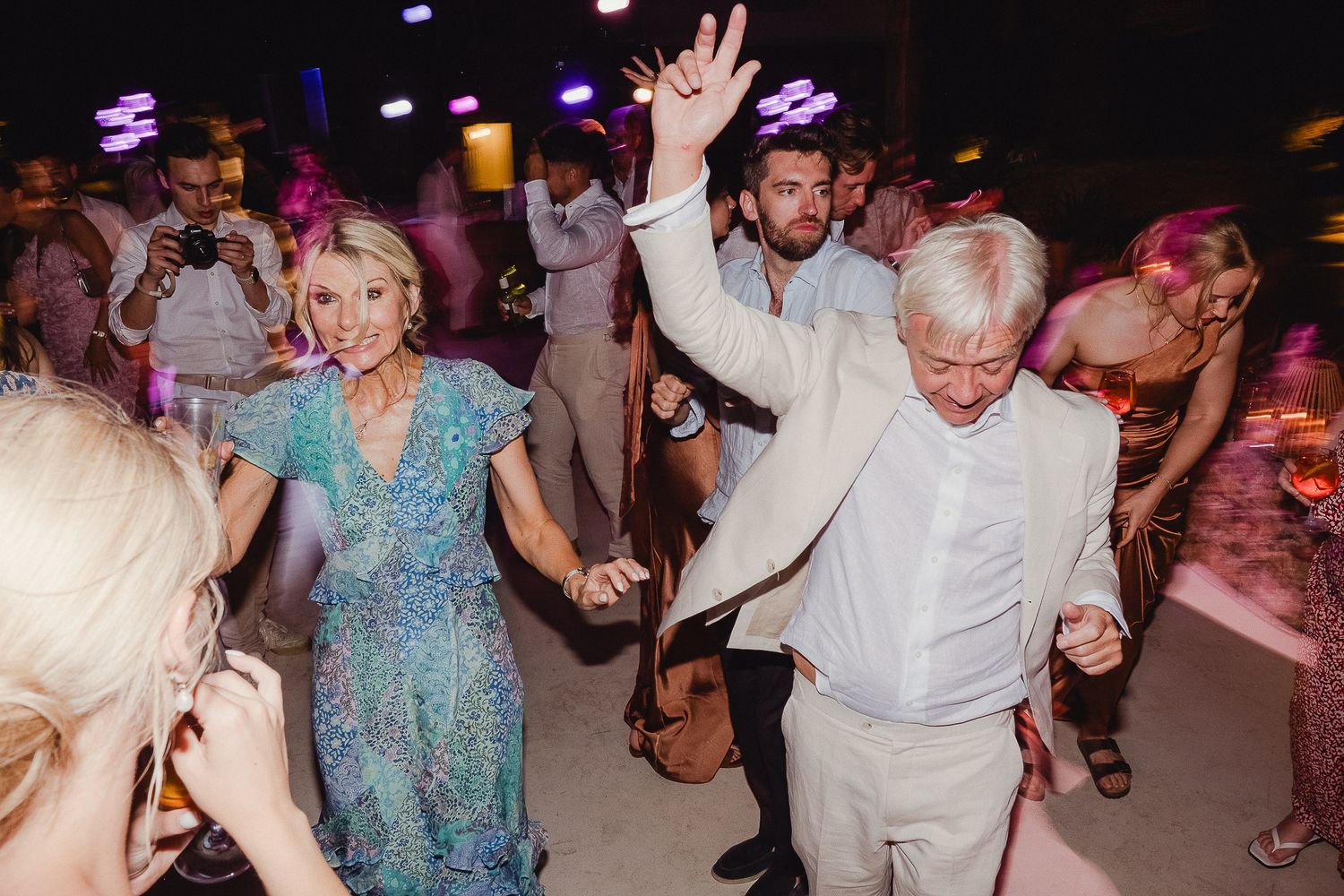 People dancing together at a lively indoor party or celebration with colorful lighting and festive atmosphere.