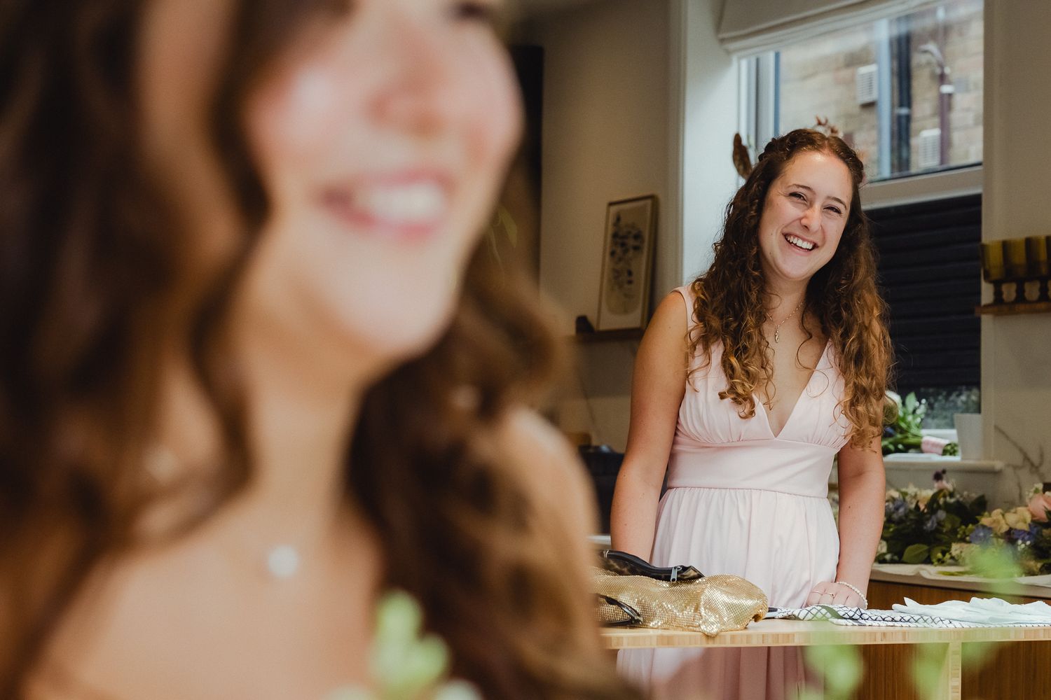 A person smiles while sitting at a table in a kitchen with warm lighting and a relaxed atmosphere.