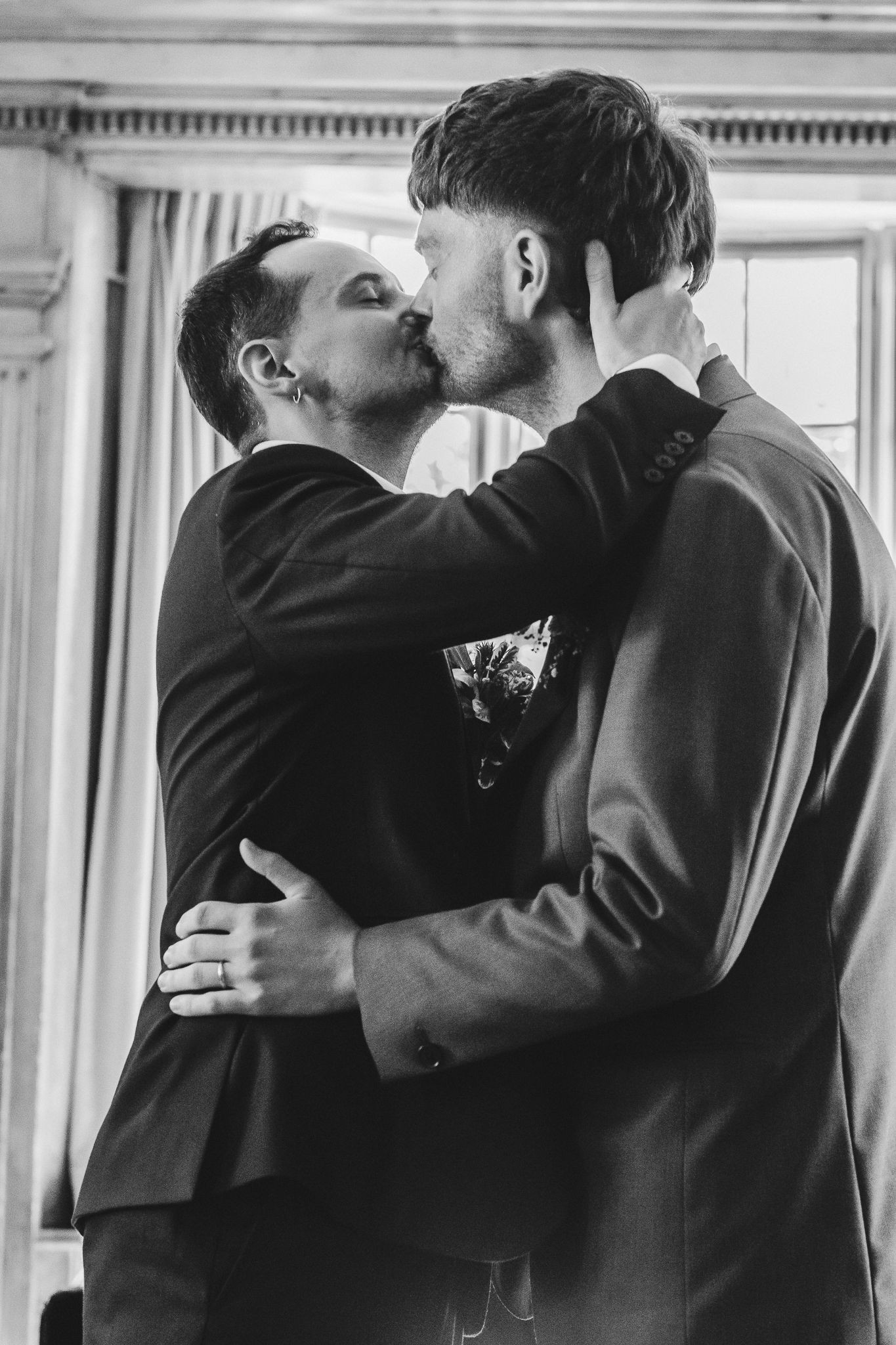 A black and white photograph shows three couples embracing and kissing in formal attire.