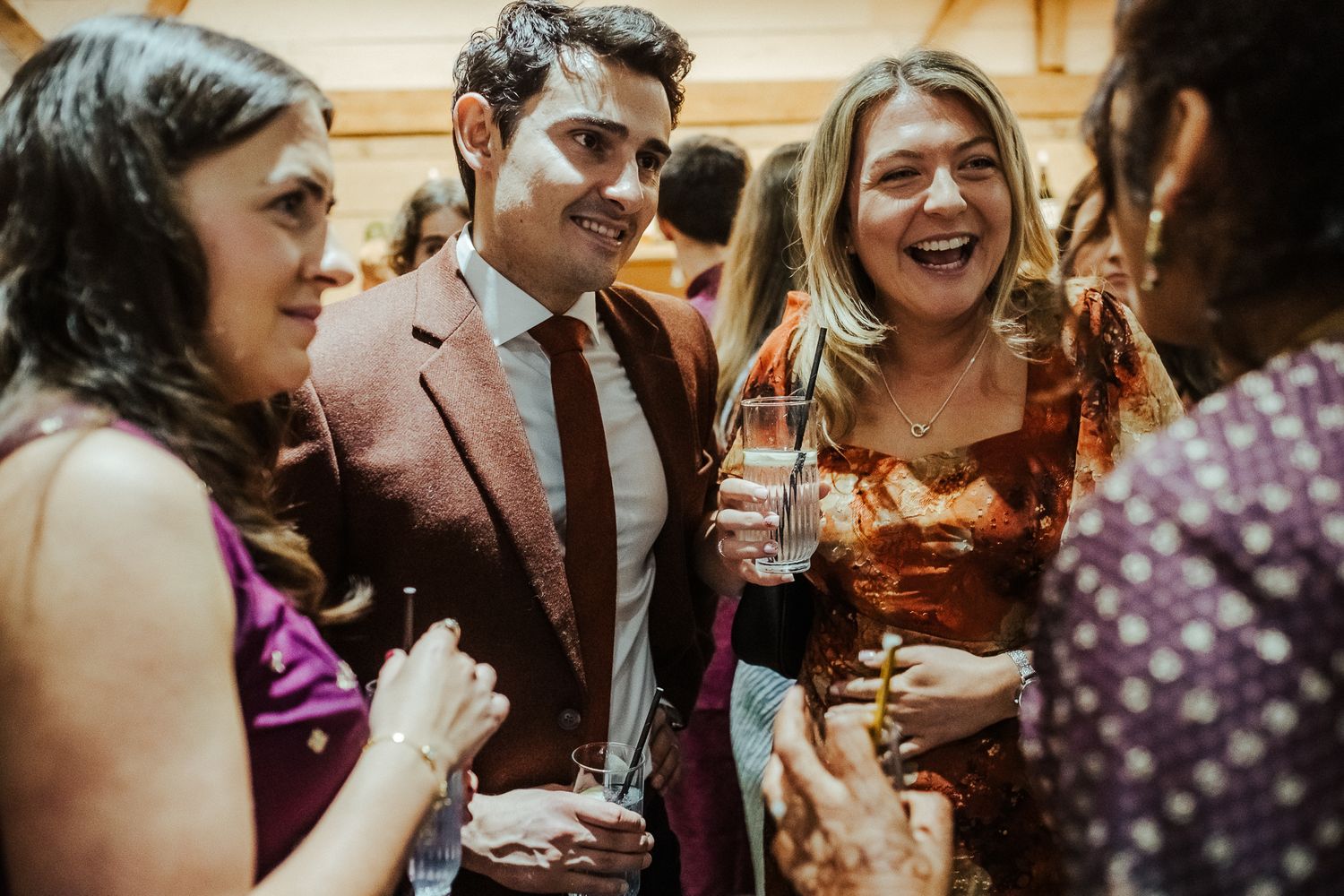 Guests enjoying drinks and laughter at a festive celebration wearing formal and traditional attire.