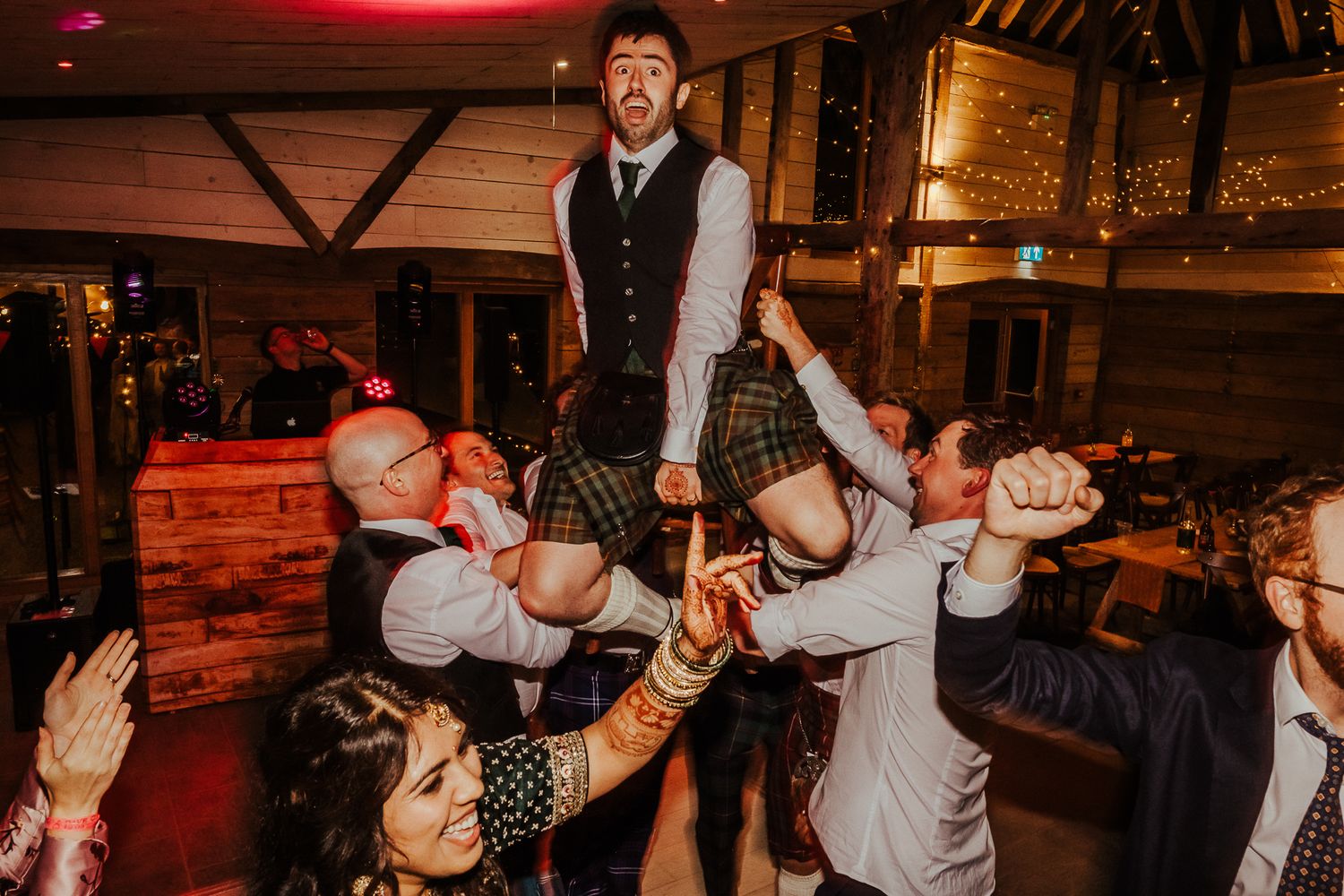 Large group of party guests dancing with arms raised on a dance floor.