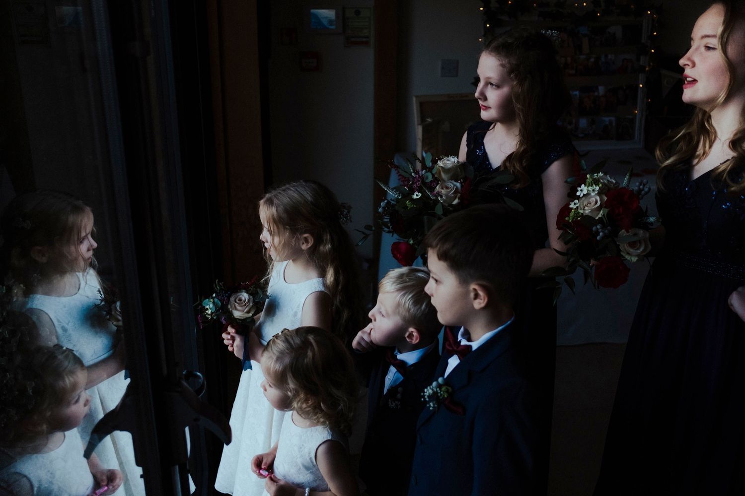 Wedding party members in formal attire gathered near a window with dramatic lighting.
