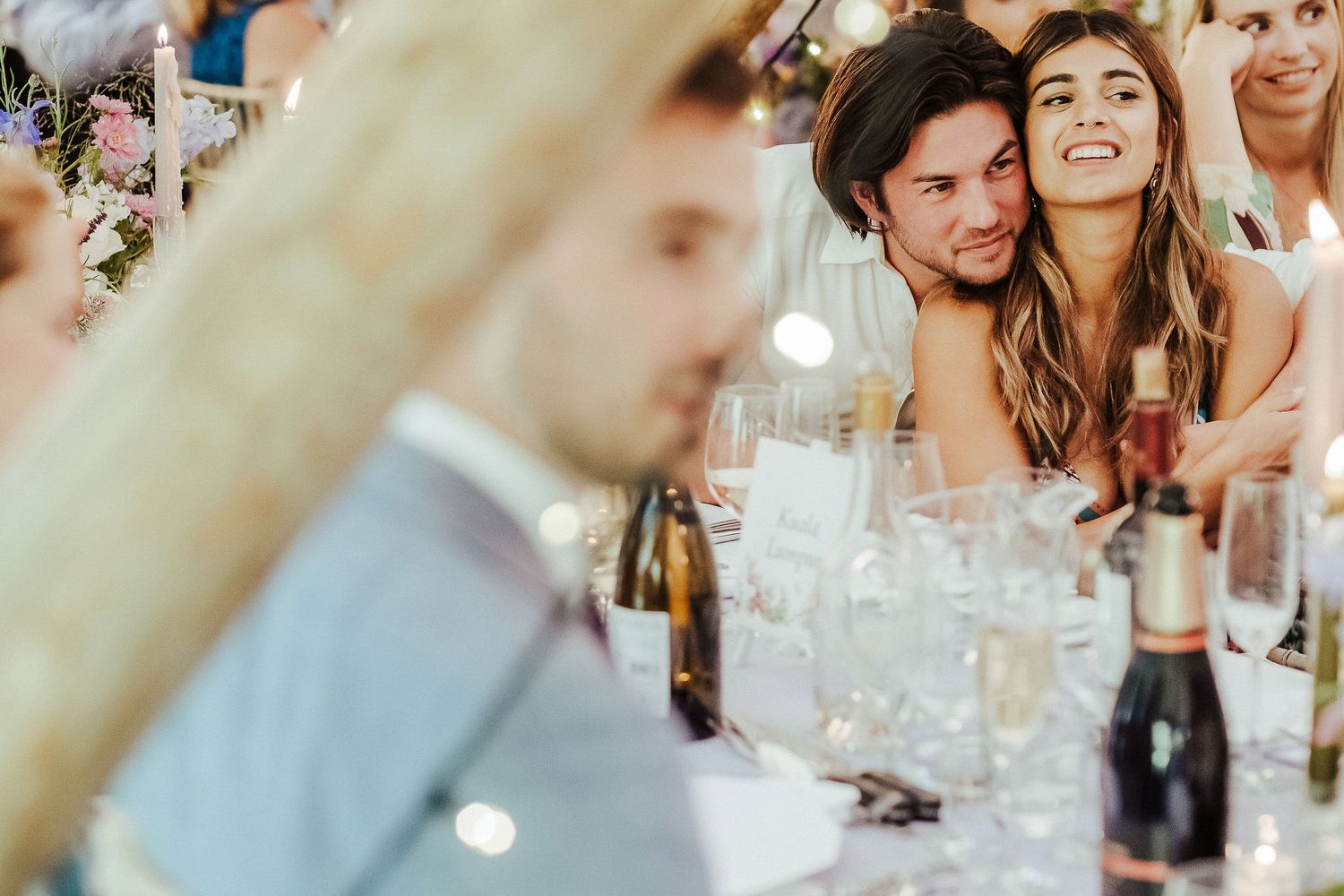 Reception guests share intimate conversation among wine glasses at wedding dinner table.