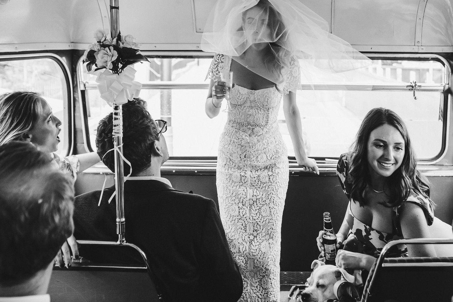 Black and white photo of wedding guests enjoying drinks and conversation inside a vehicle.