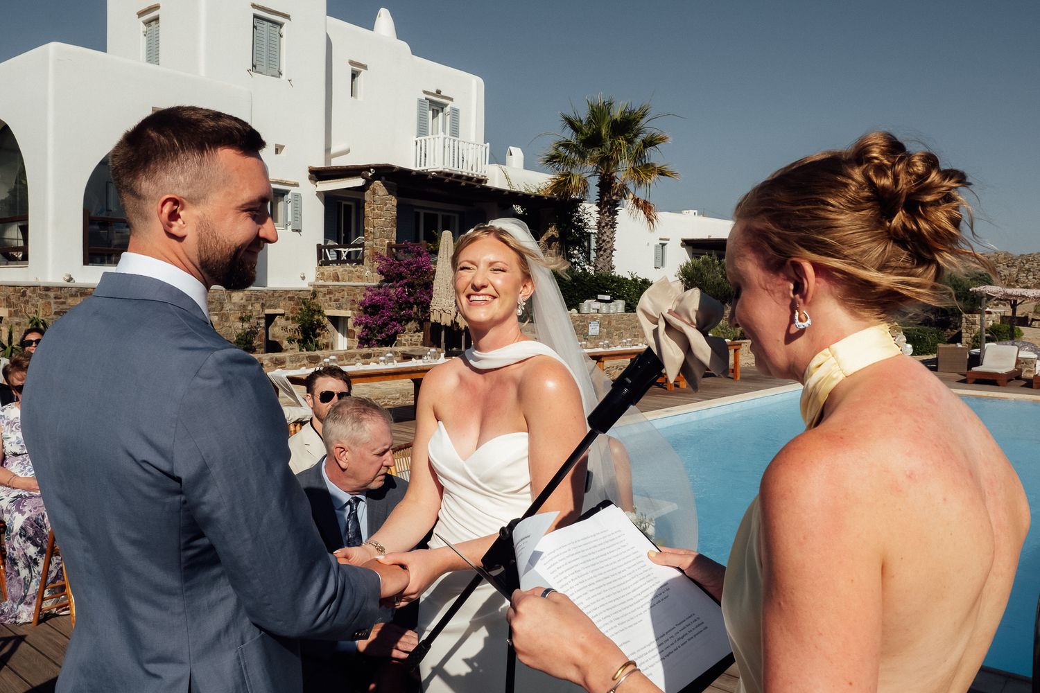 Bride and groom exchanging vows with officiant at outdoor wedding ceremony by pool in Mykonos, Greece.