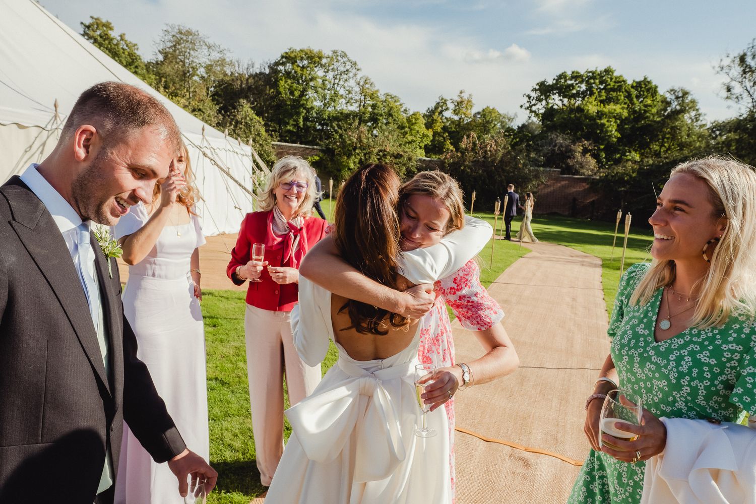 Wedding guests enjoy a playful moment during an outdoor celebration on a sunny day at a garden venue.