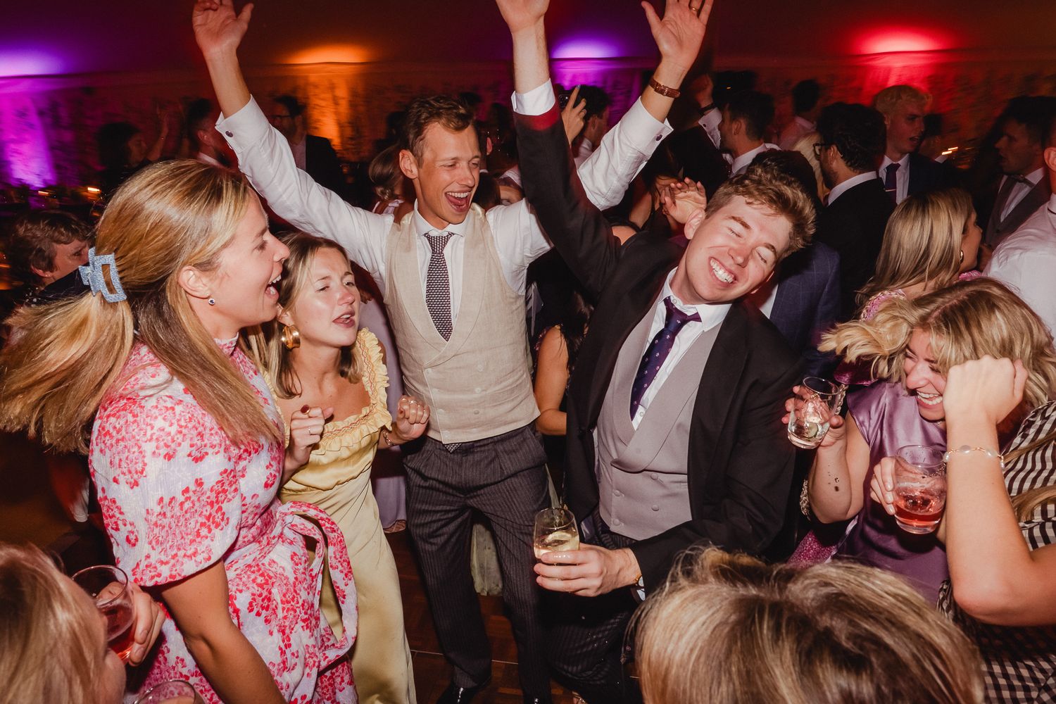 People dancing and celebrating at a lively party with colorful purple and red lighting in the background.