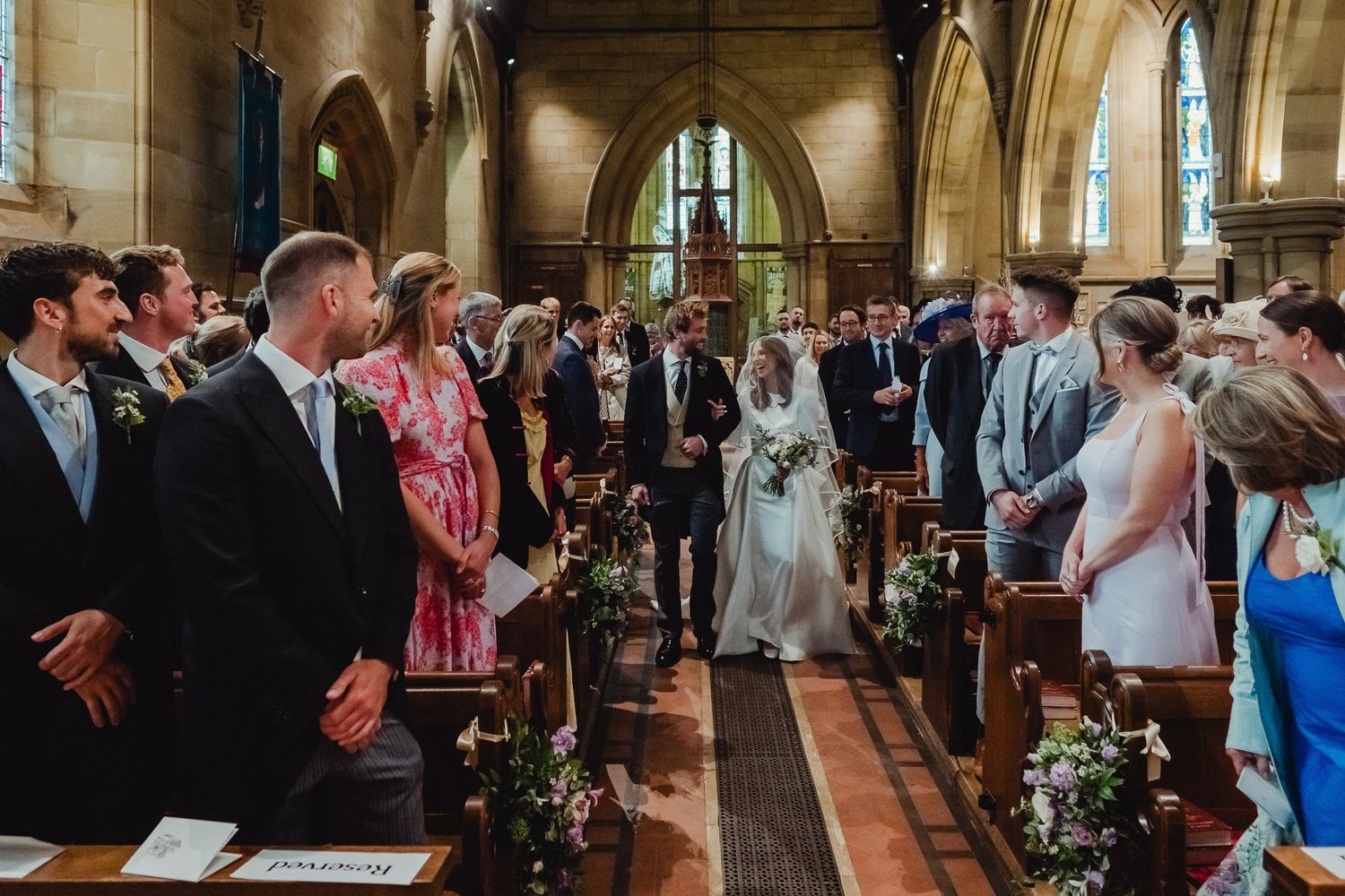 Wedding ceremony inside a traditional church with vaulted ceilings and stained glass windows as guests look on.