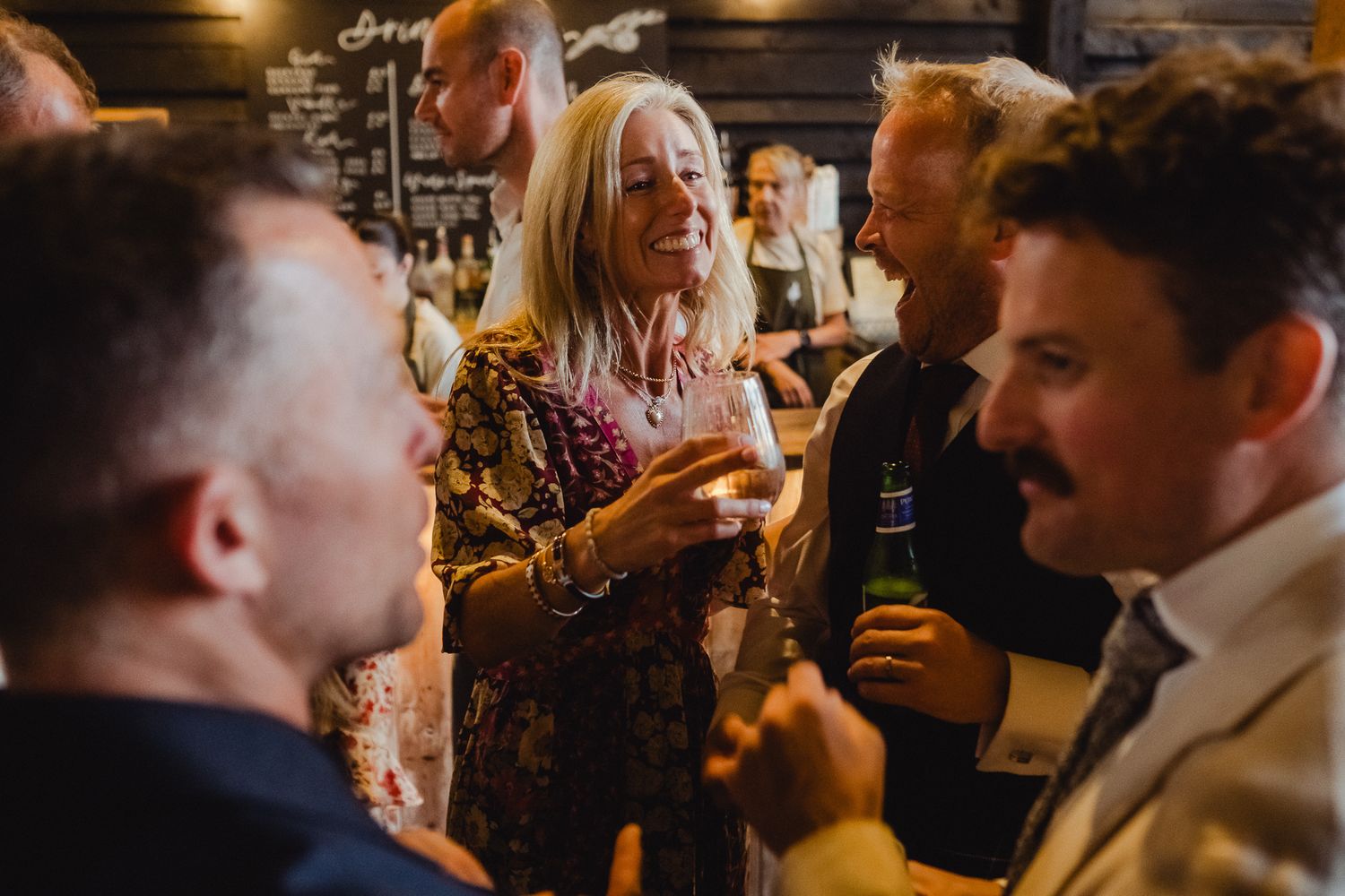 A group of people socialize and enjoy drinks at a dimly lit bar or pub with warm lighting.