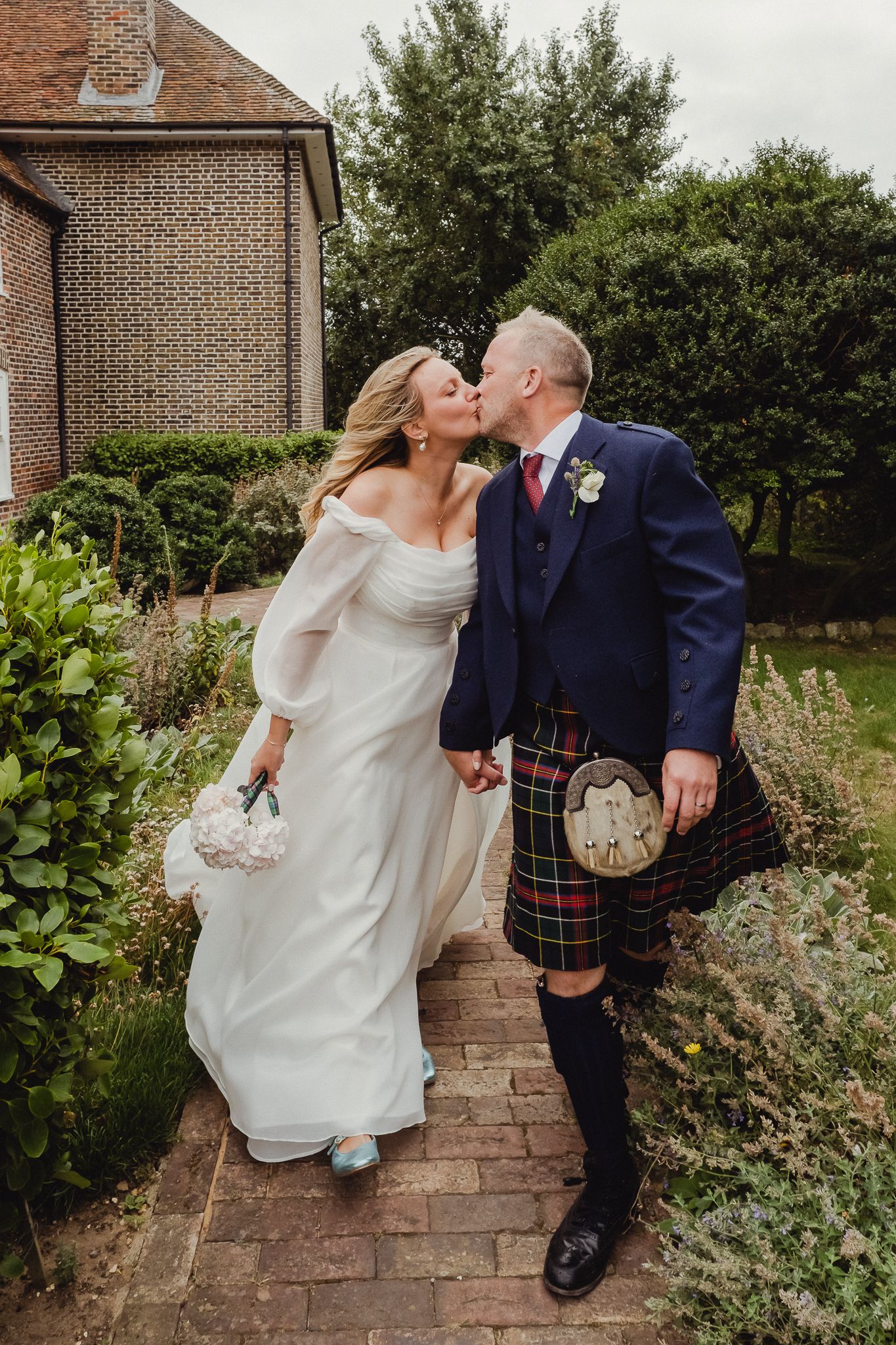 A romantic wedding couple shares intimate moments on brick steps surrounded by lush garden greenery.