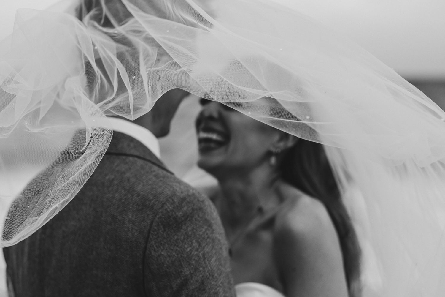 A black and white wedding photo showing the bride and groom sharing an intimate moment under a flowing veil.