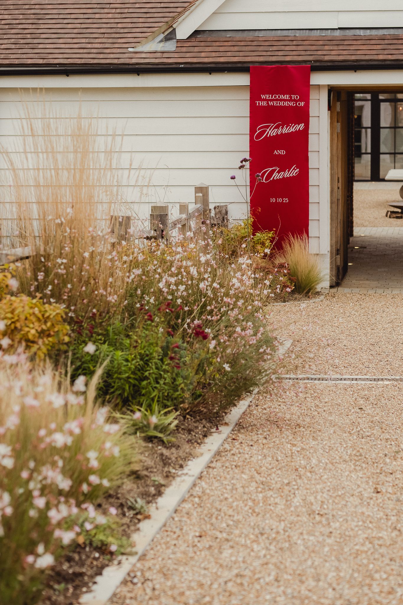 White building exterior with red door signs and delicate wildflowers growing along gravel pathway.