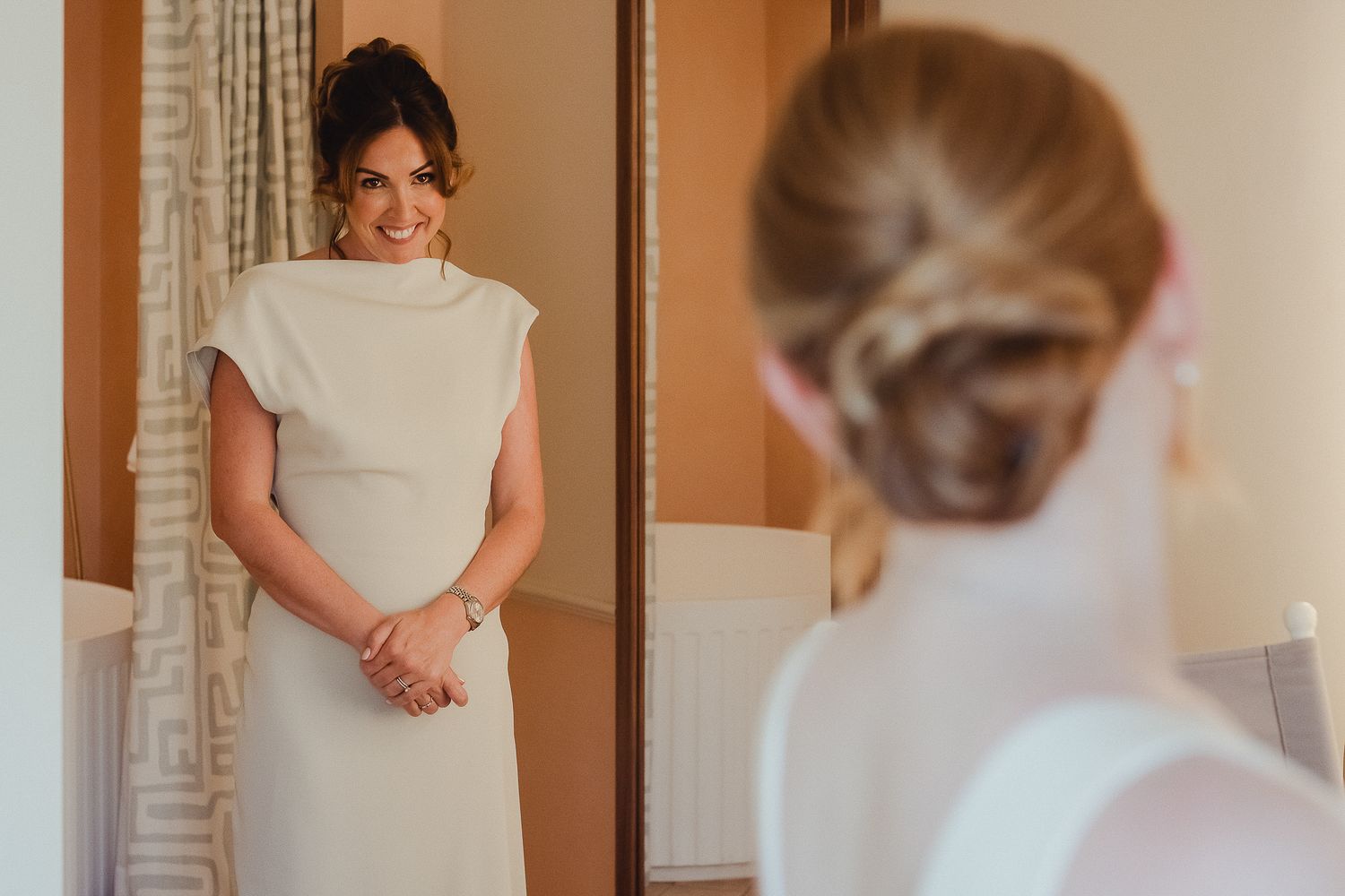 A person in a white dress adjusts their outfit in a mirror while getting ready for a special occasion.