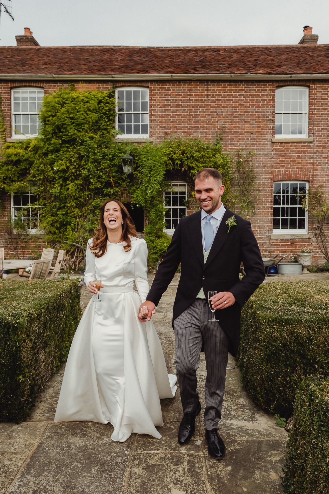 A series of wedding photos showing a couple walking and laughing together along a brick building with manicured hedges.
