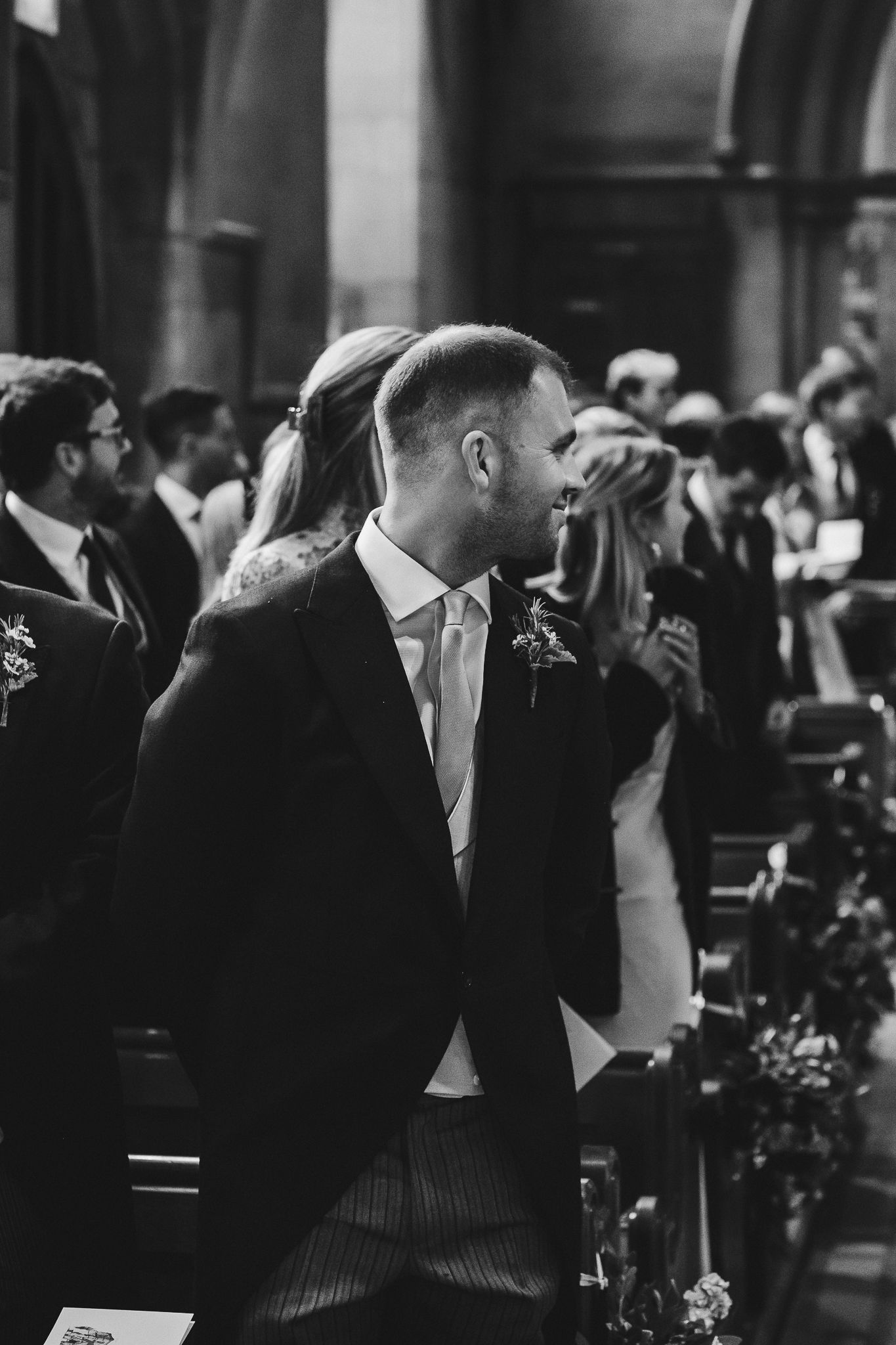 Black and white photograph of a crowded formal event with people in elegant attire mingling in an indoor venue.