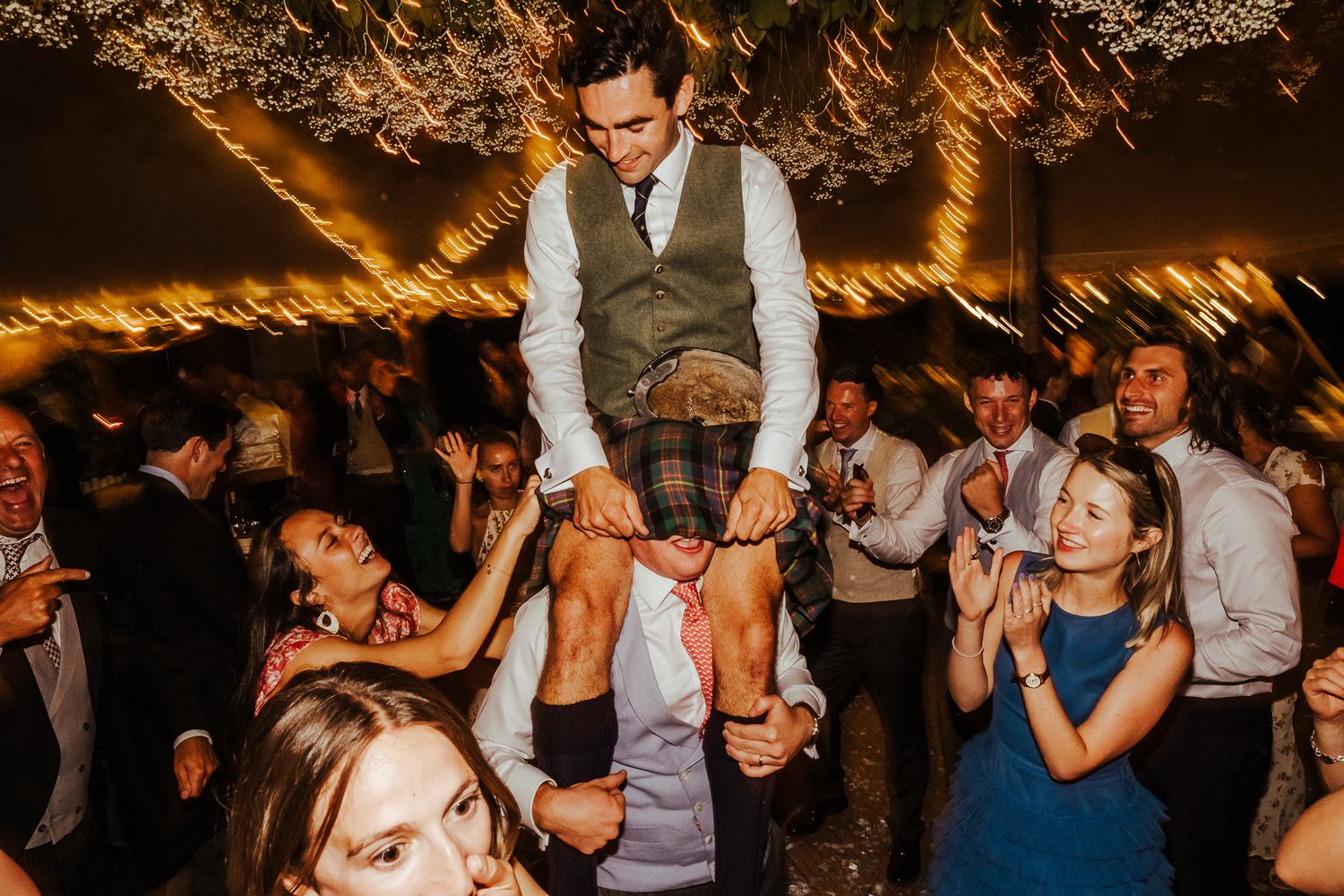 Wedding guest being lifted up by others during an energetic dance party celebration.