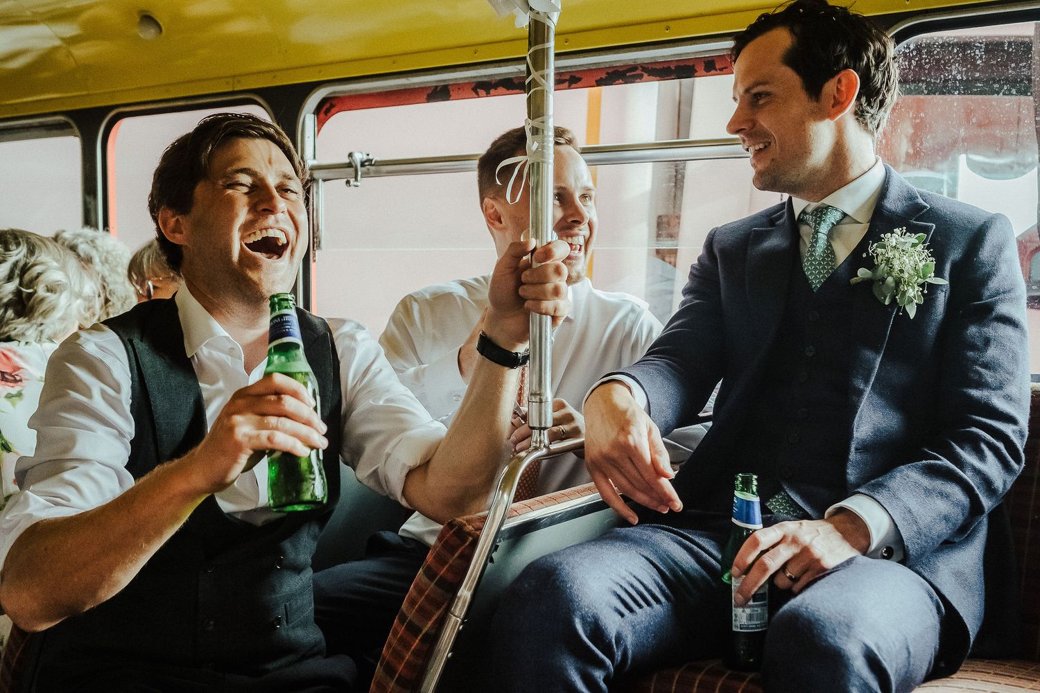 Wedding party laughing and drinking together in a casual celebration moment.