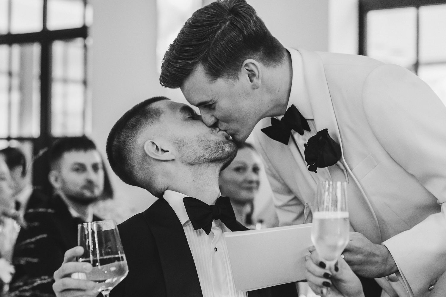 Wedding guests enjoy a lively reception celebration with champagne toasts and laughter at an indoor venue.