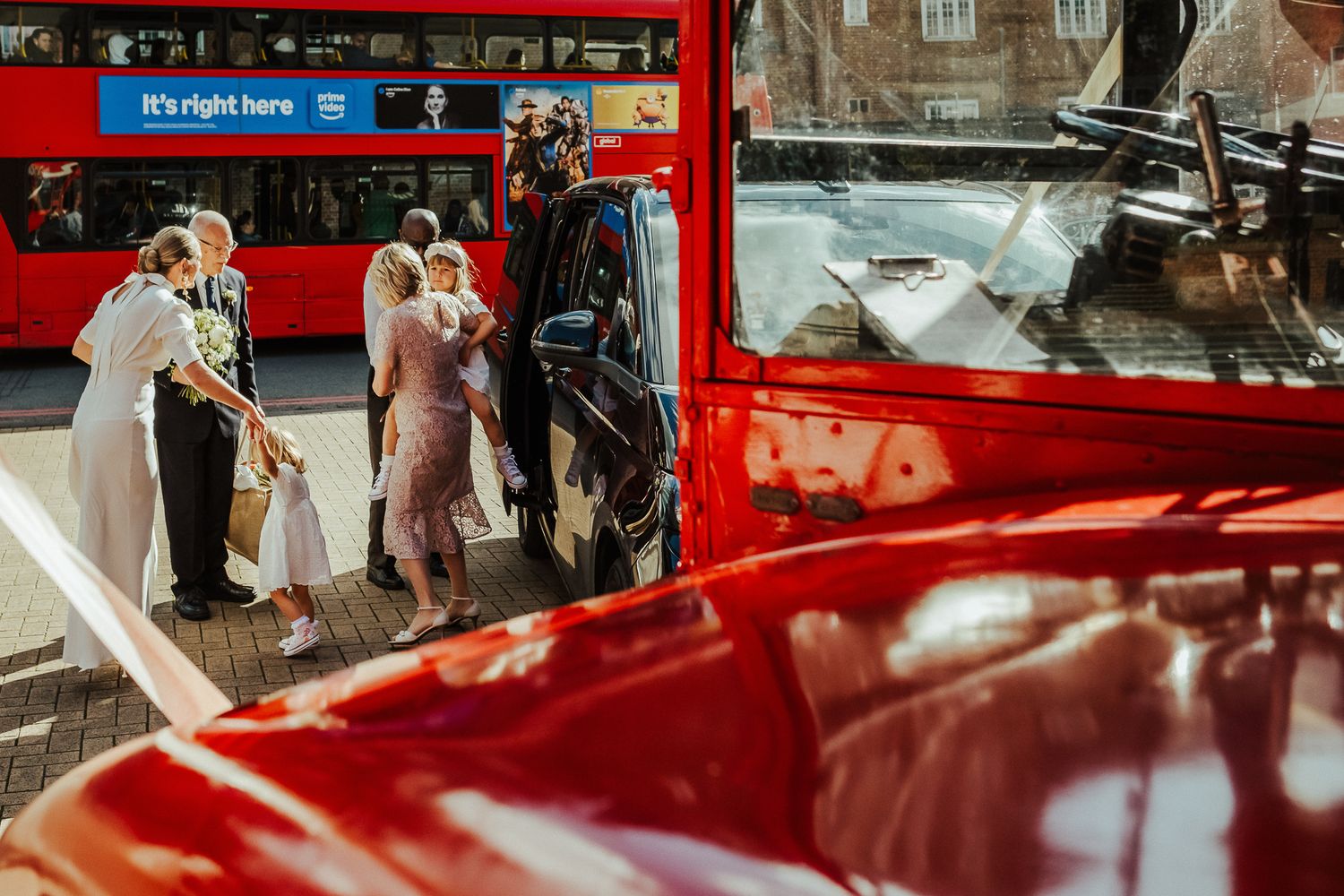 Wedding guest signs a bright red classic car decorated with 'Just Married' text and traditional ornaments.
