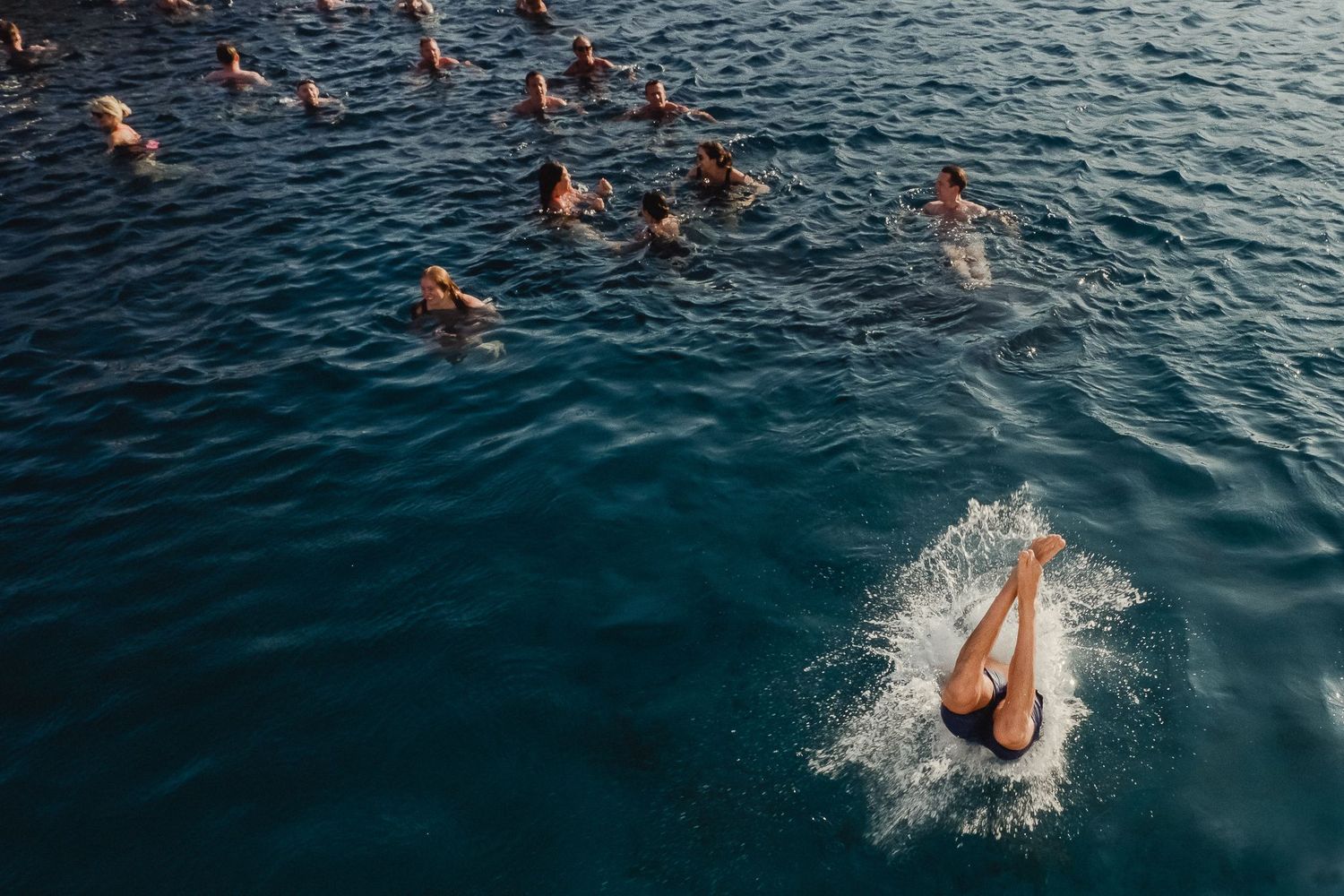 Swimmers dive and splash in deep blue Mediterranean waters on a sunny summer day.