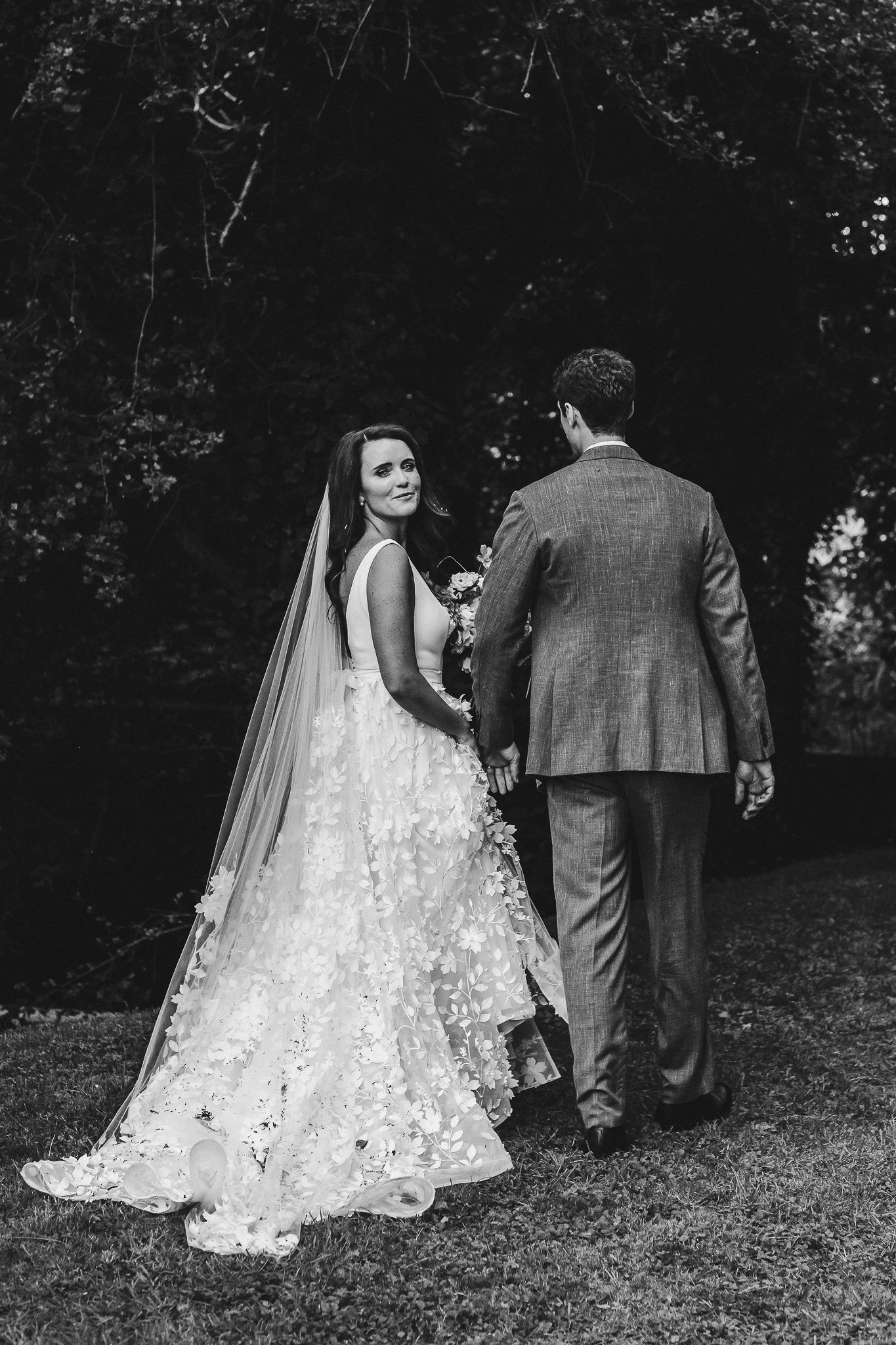 Black and white portrait of bride and groom walking together in garden setting.