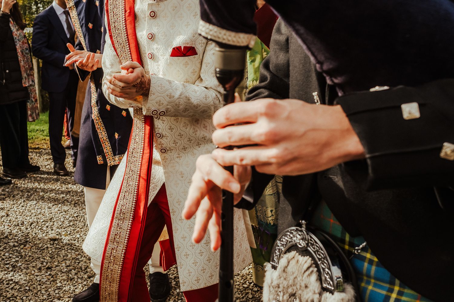 Close-up of hands holding drinks with Scottish kilts visible in the wedding celebration.