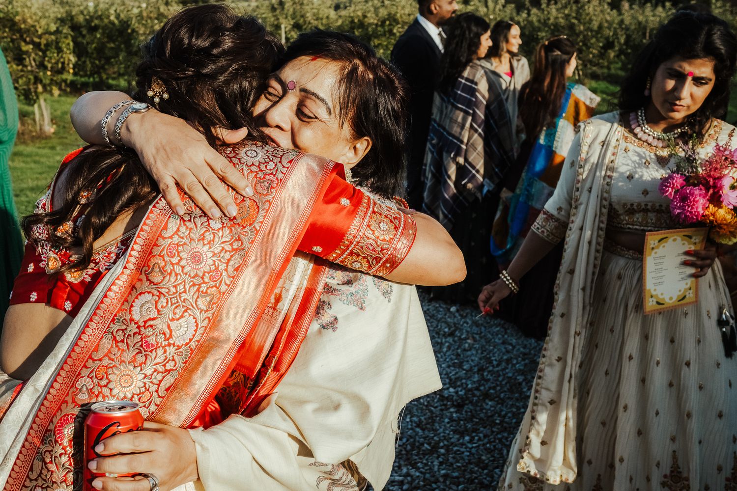 Heartfelt hug between wedding guests wearing traditional Indian attire at an outdoor celebration.