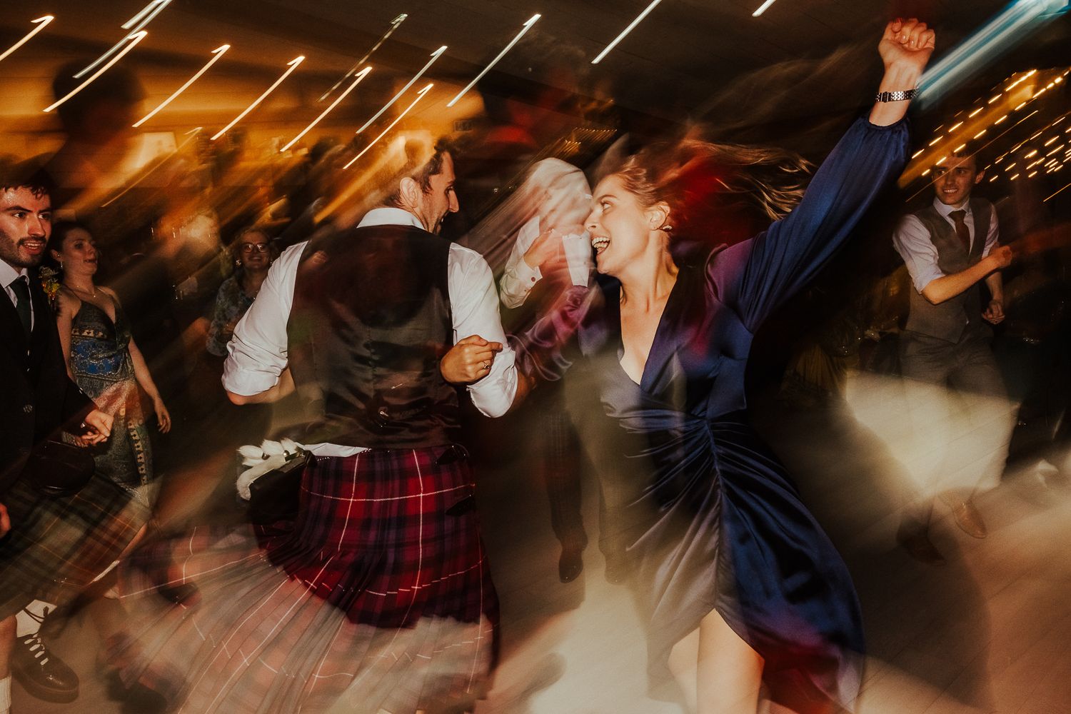 Energetic dance party with guests wearing kilts and formal attire.