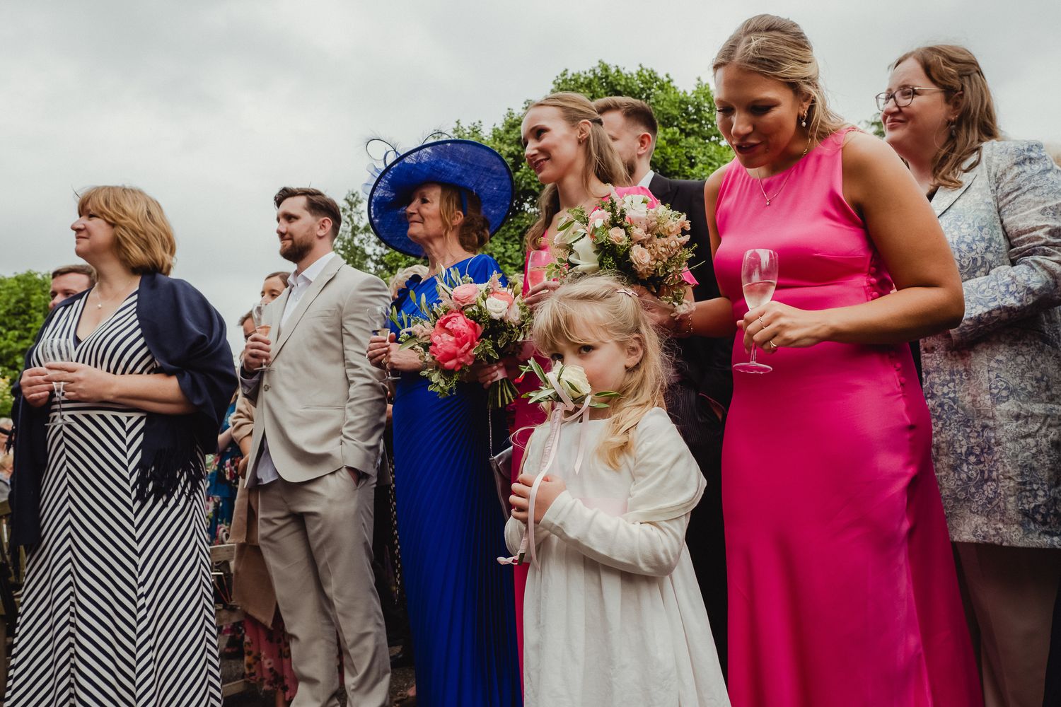 Wedding party members in colorful dresses and suits walk and gather together outdoors in a candid moment.