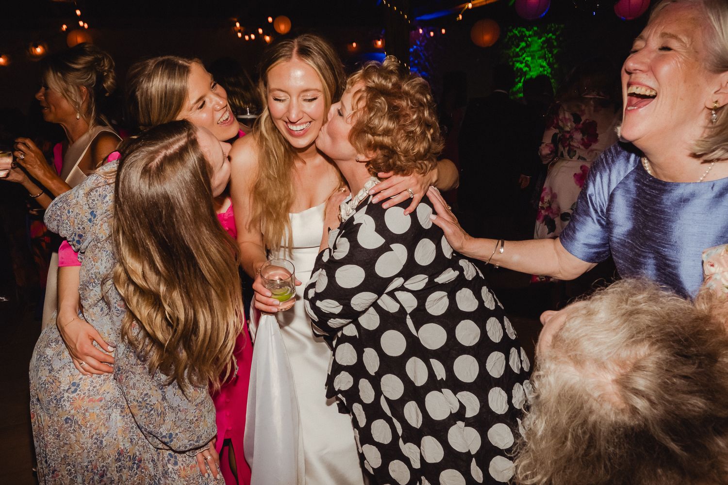 People having fun and dancing together at a vibrant wedding reception with colorful ambient lighting.