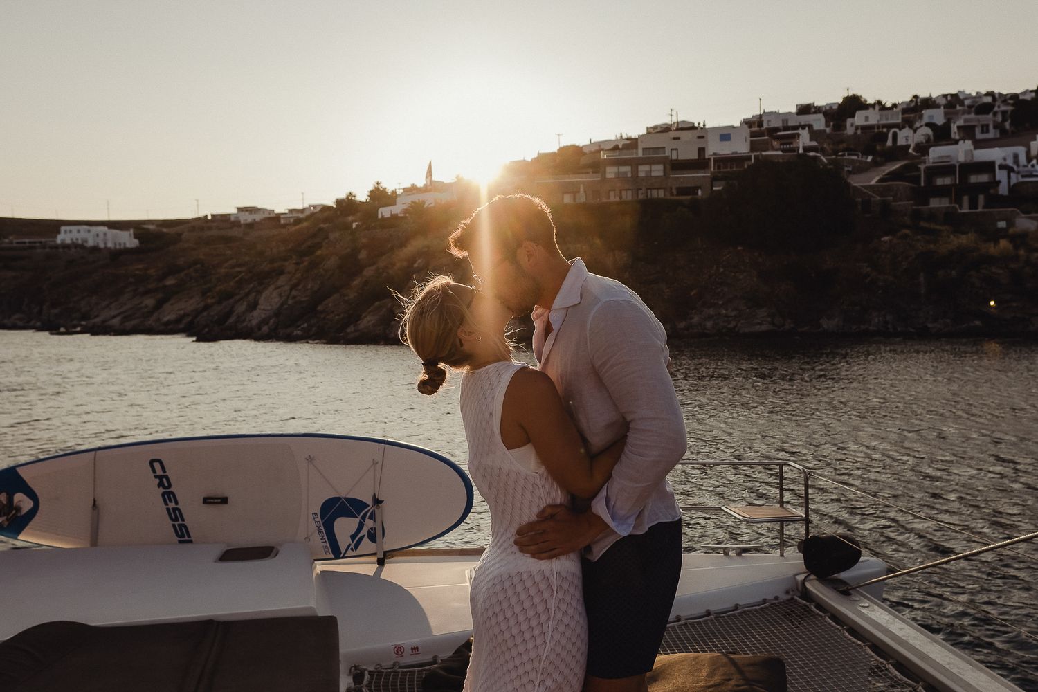 Two people enjoy a romantic sunset moment on a boat deck overlooking a tranquil harbor.