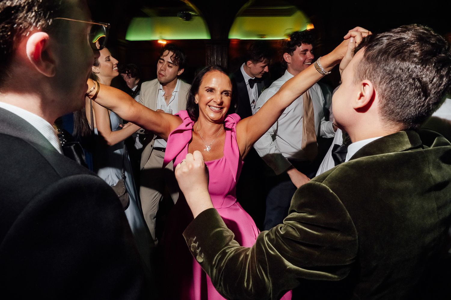 Woman in pink dress dancing joyfully with guests at a lively wedding reception party.