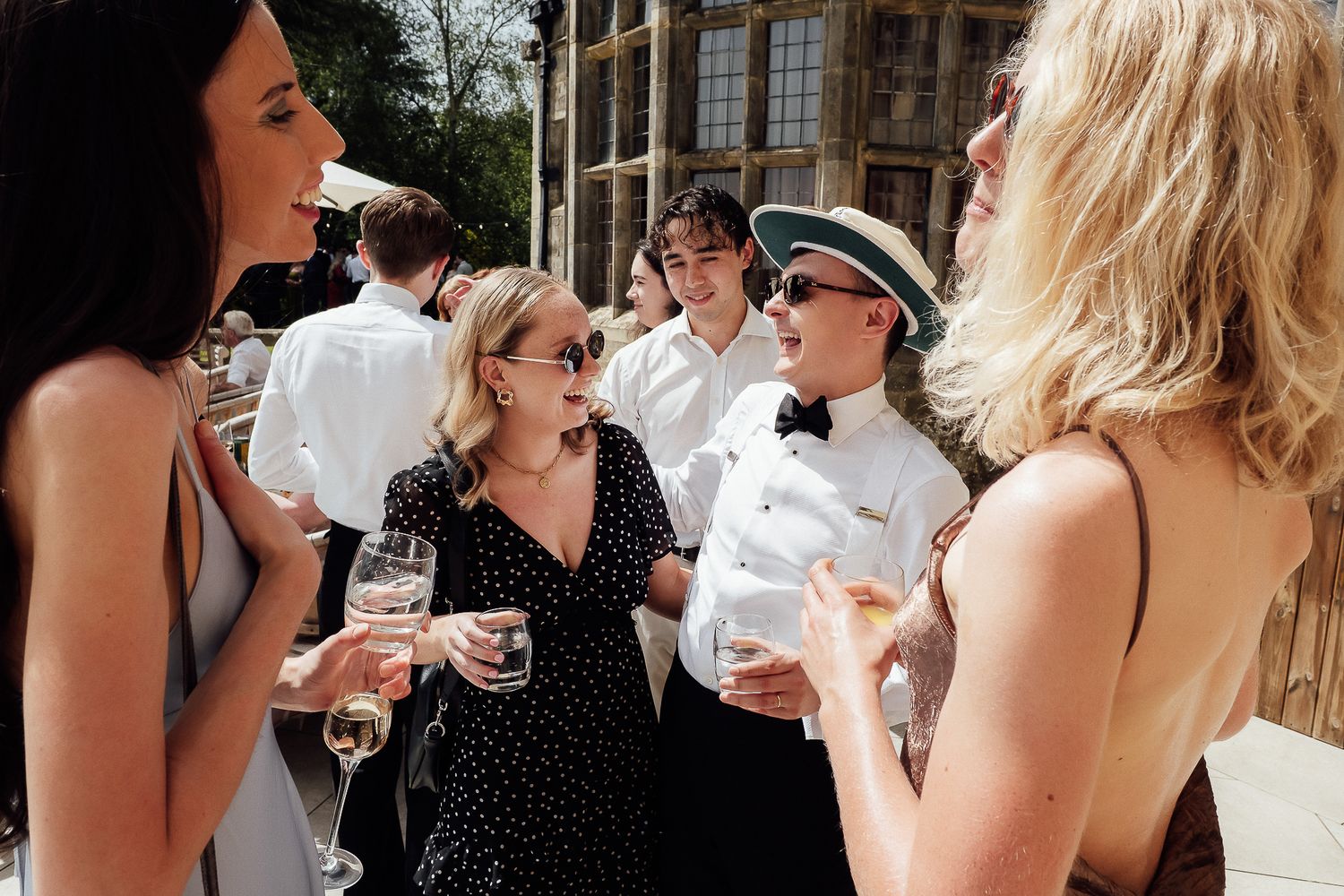 Elegant outdoor social gathering with guests in formal attire enjoying champagne at a sunny garden party.