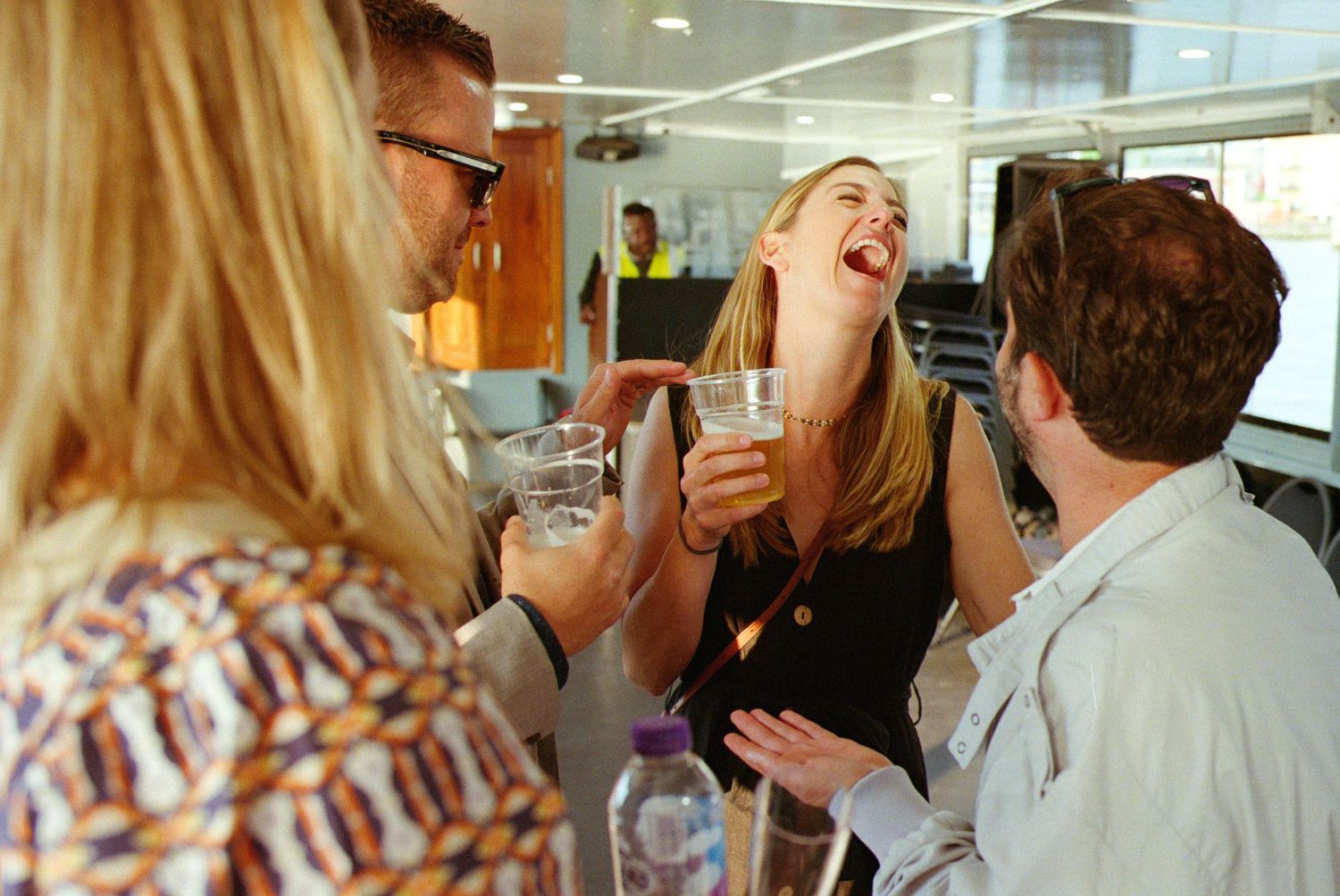 Group of colleagues laughing and socializing at an office party, holding drinks and enjoying conversation.