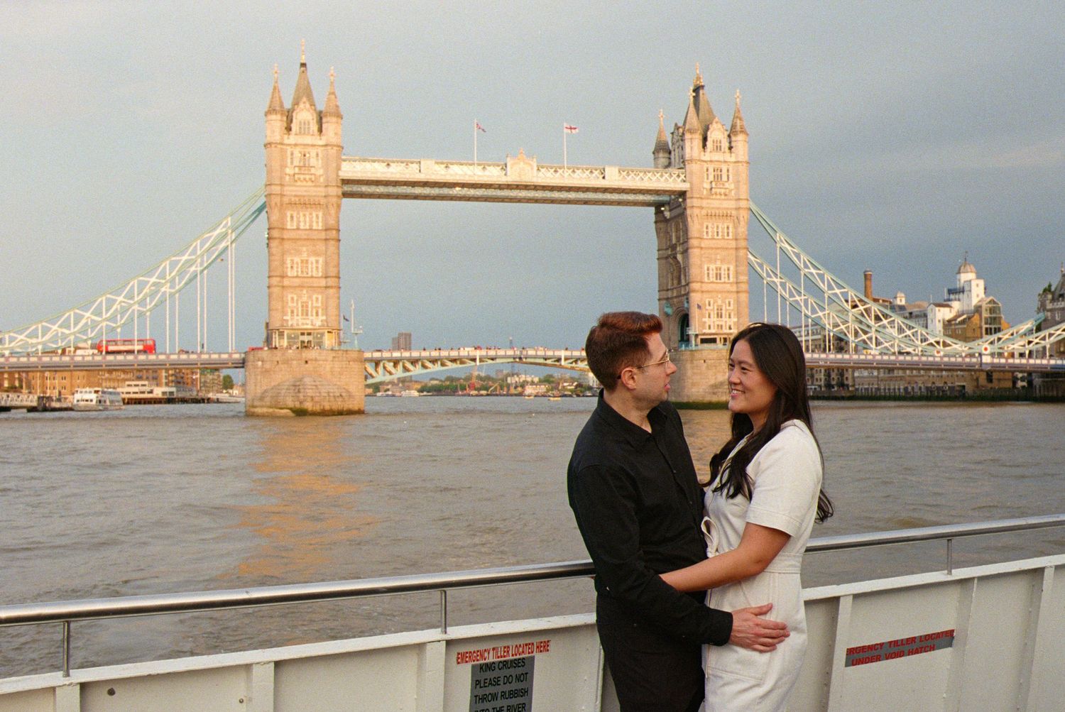 Couple embracing on a boat with Tower Bridge over the River Thames in London in the background.