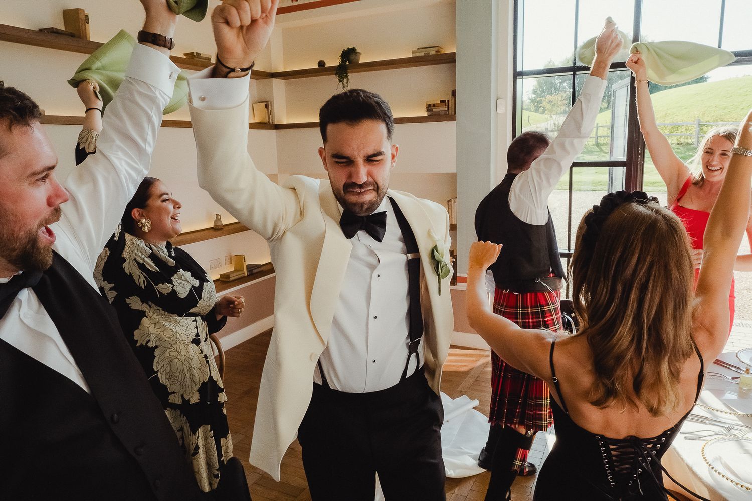 Wedding party celebrates with raised glasses and joyful expressions during a toast at an indoor reception.