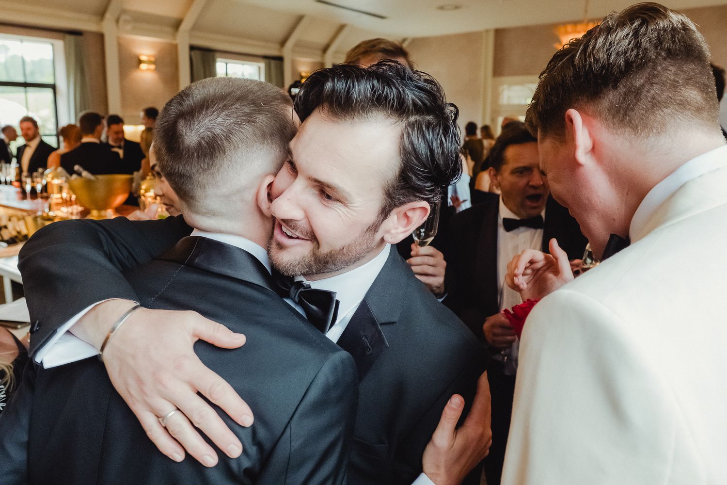 Guests embrace and celebrate at a formal wedding reception in an elegant indoor venue.
