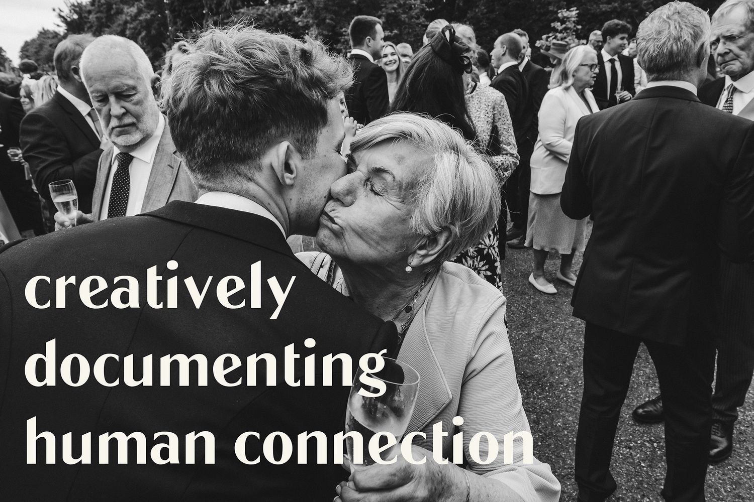 Black and white photo of an elderly woman kissing a young man at a wedding reception outdoors.