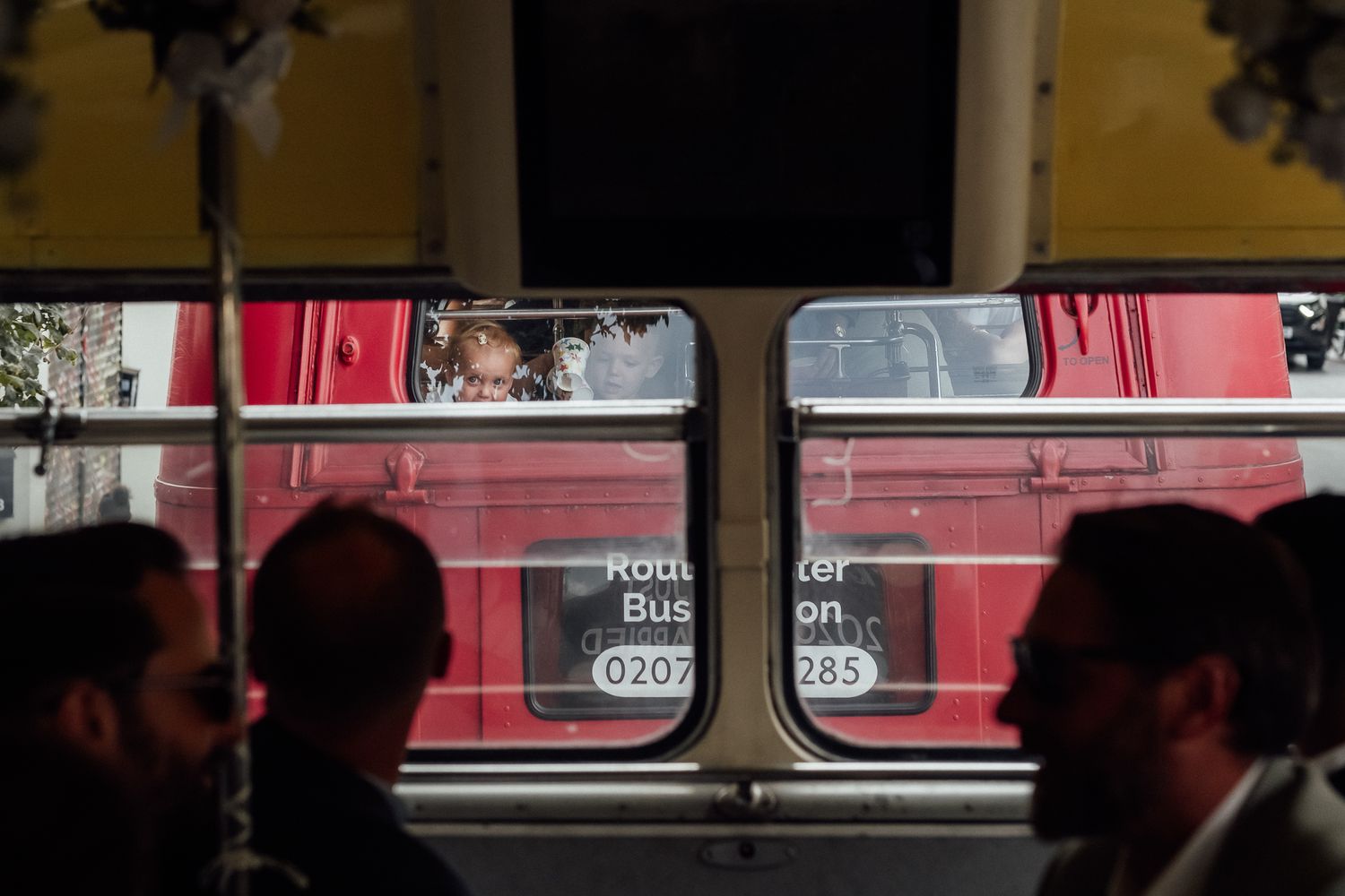 Silhouetted passengers inside a vintage bus look through windows at a red Routemaster bus parked outside with a phone number on its side.
