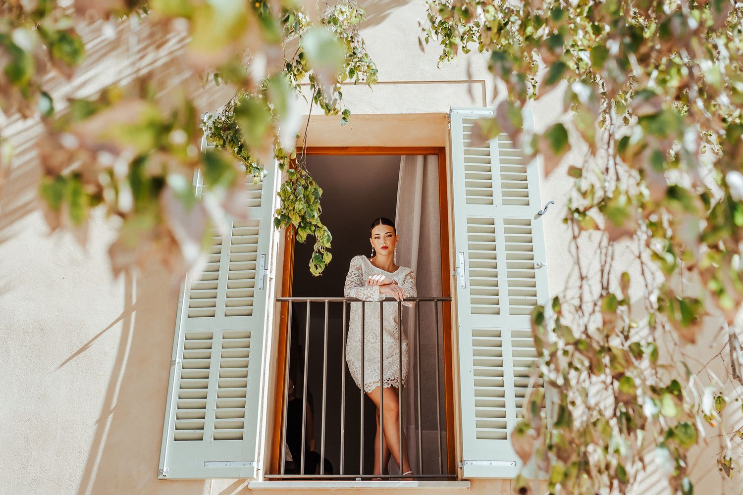 Person standing at a balcony window with white shutters framed by delicate pink spring blossoms.