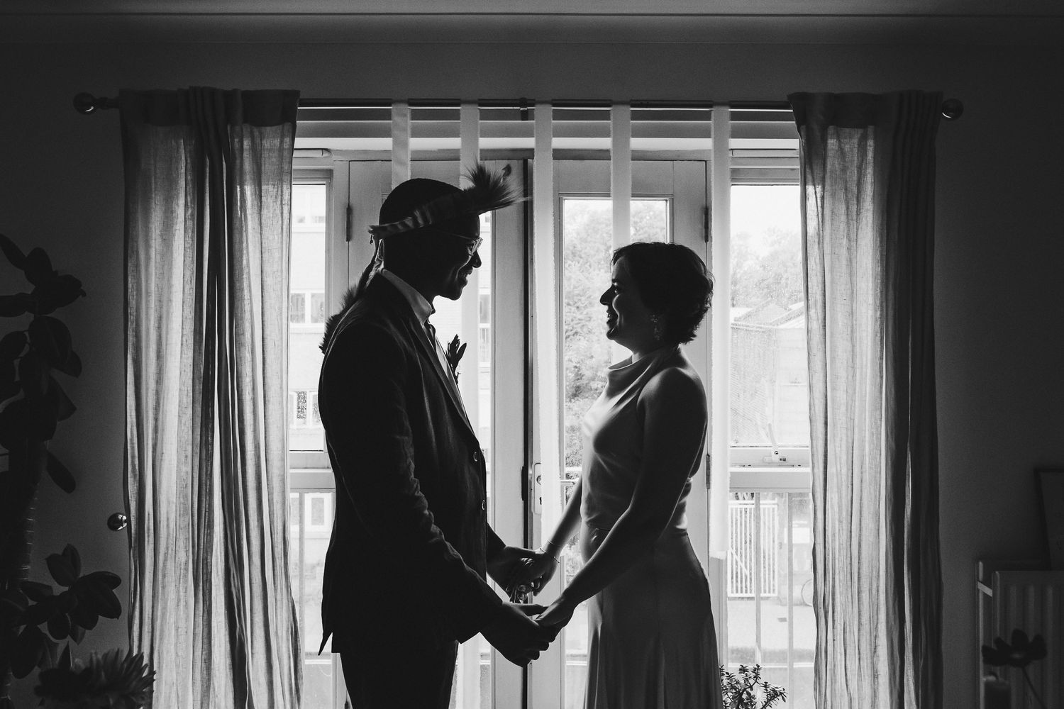 A silhouetted couple holds hands while standing by a window in a romantic black and white moment.