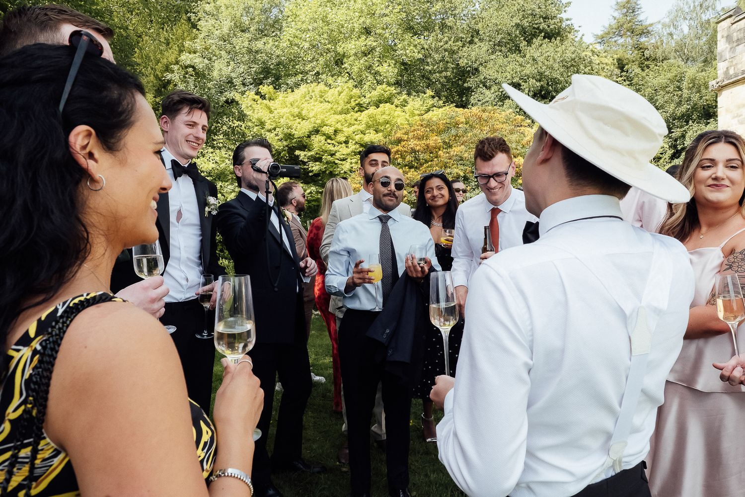 Elegantly dressed guests mingling outdoors at a garden party, holding champagne glasses amid lush greenery.
